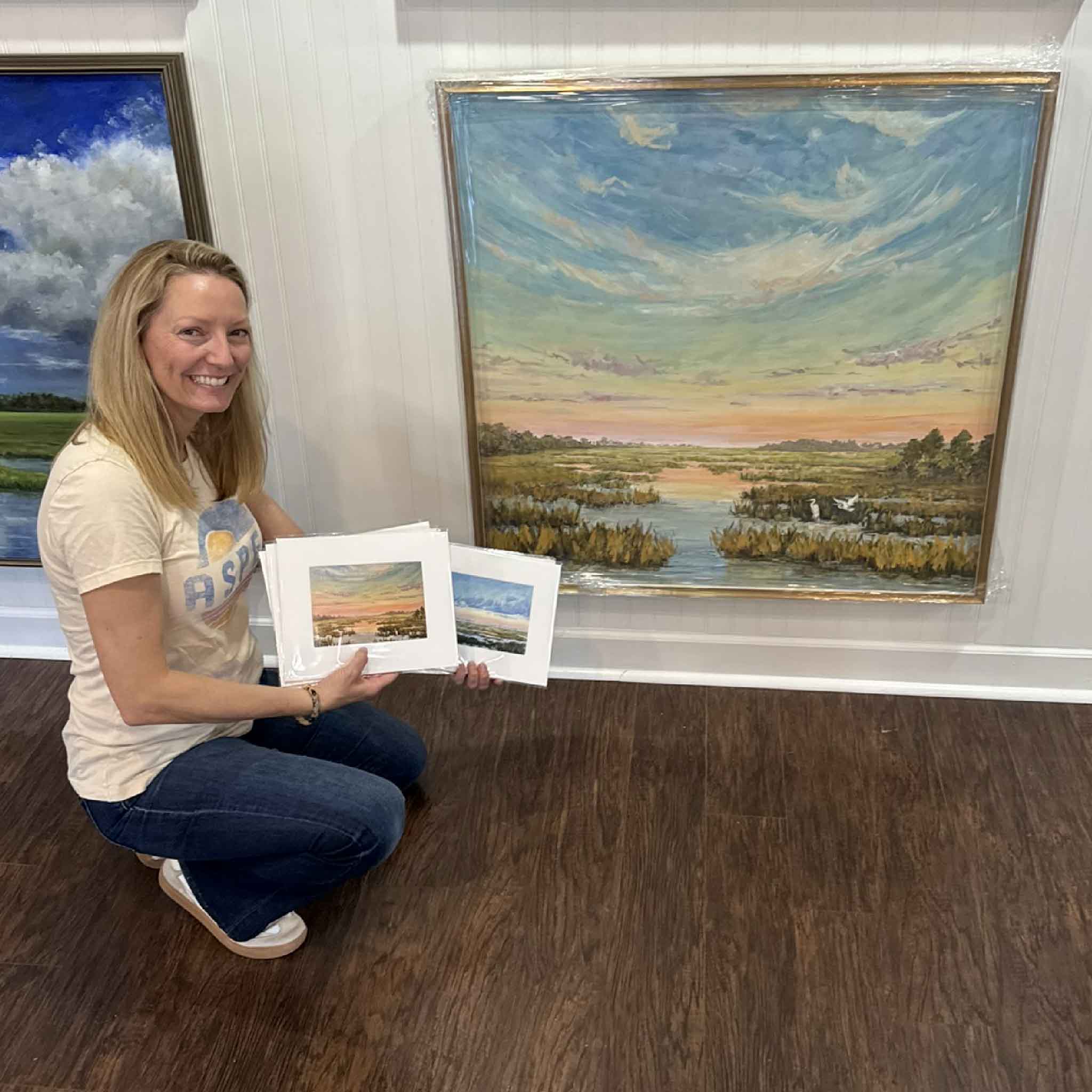 Jeanne O’Neal with original Marsh at First Light oil painting alongside enhanced giclée prints, demonstrating the hand-painted details and Lowcountry marsh scene inspiration, pictured at the old Gray Man Gallery next to Bistro 217