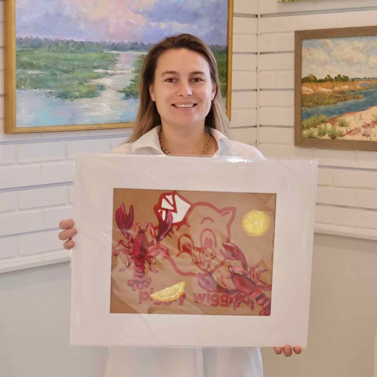 Gray Man Gallery team member holding Lobstahs & Lemons by local artist Jenny Reynolds, an original acrylic painting featuring red lobsters and bright yellow lemons painted over the classic Piggly Wiggly logo on an authentic brown paper grocery bag. The matted coastal artwork is photographed inside Gray Man Gallery in Pawleys Island, South Carolina.