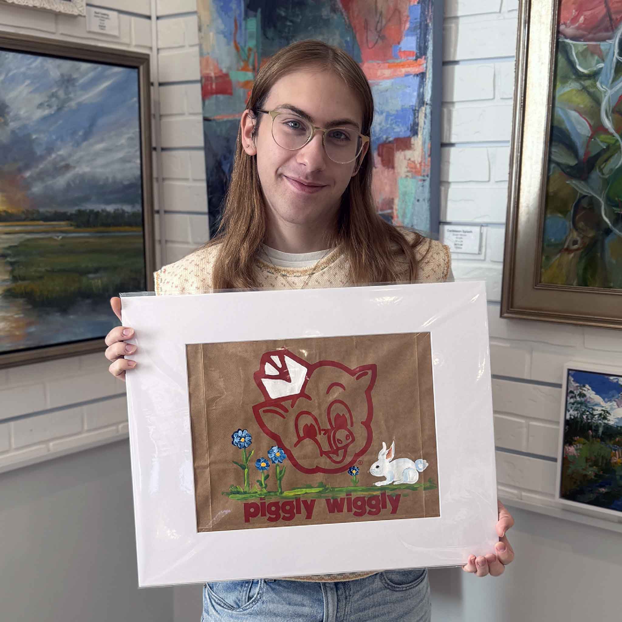 Hand-painted Piggly Wiggly grocery bag artwork by local artist Jenny Reynolds displayed at Gray Man Gallery in Pawleys Island, showing scale and presentation of the matted original featuring a bunny and blue blooms.