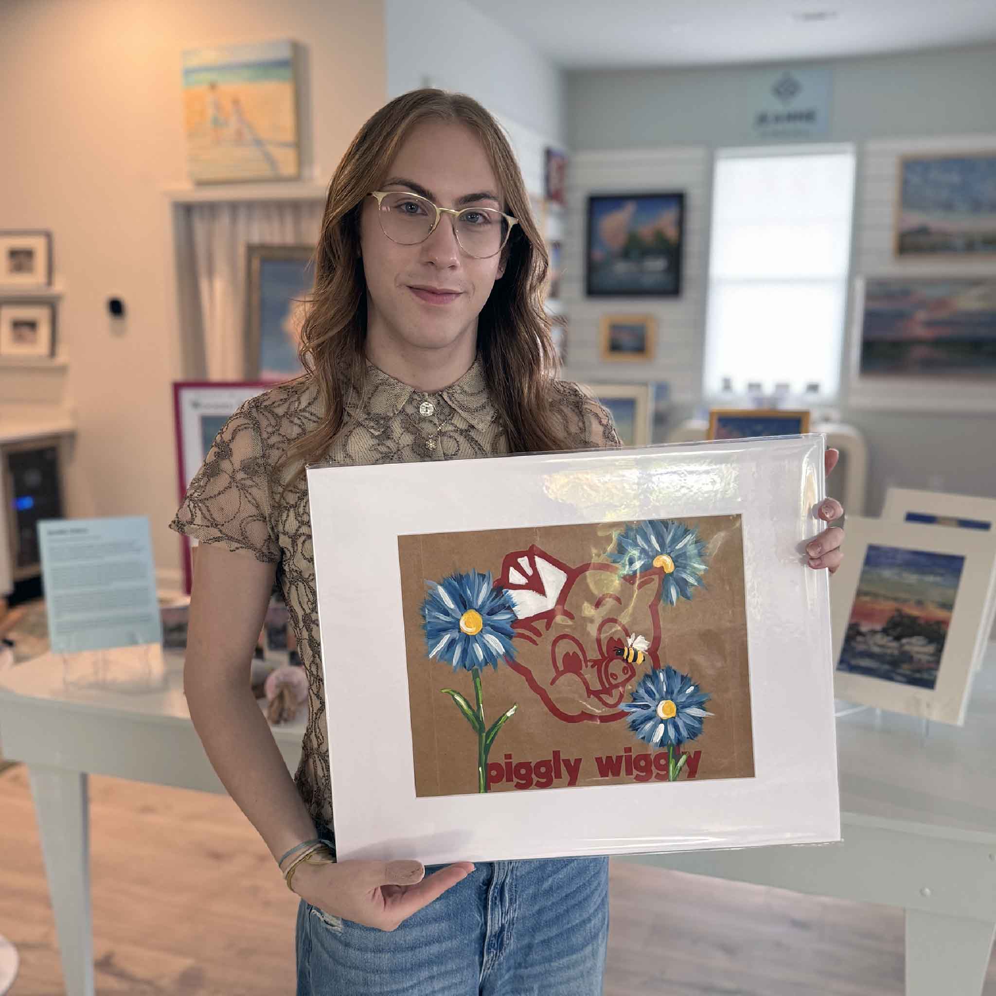 Alex holding “Piggly Wiggly: Blue Blooms & Bee,” an original Jenny Reynolds painting on a Piggly Wiggly grocery bag featuring blue flowers and a bee.
