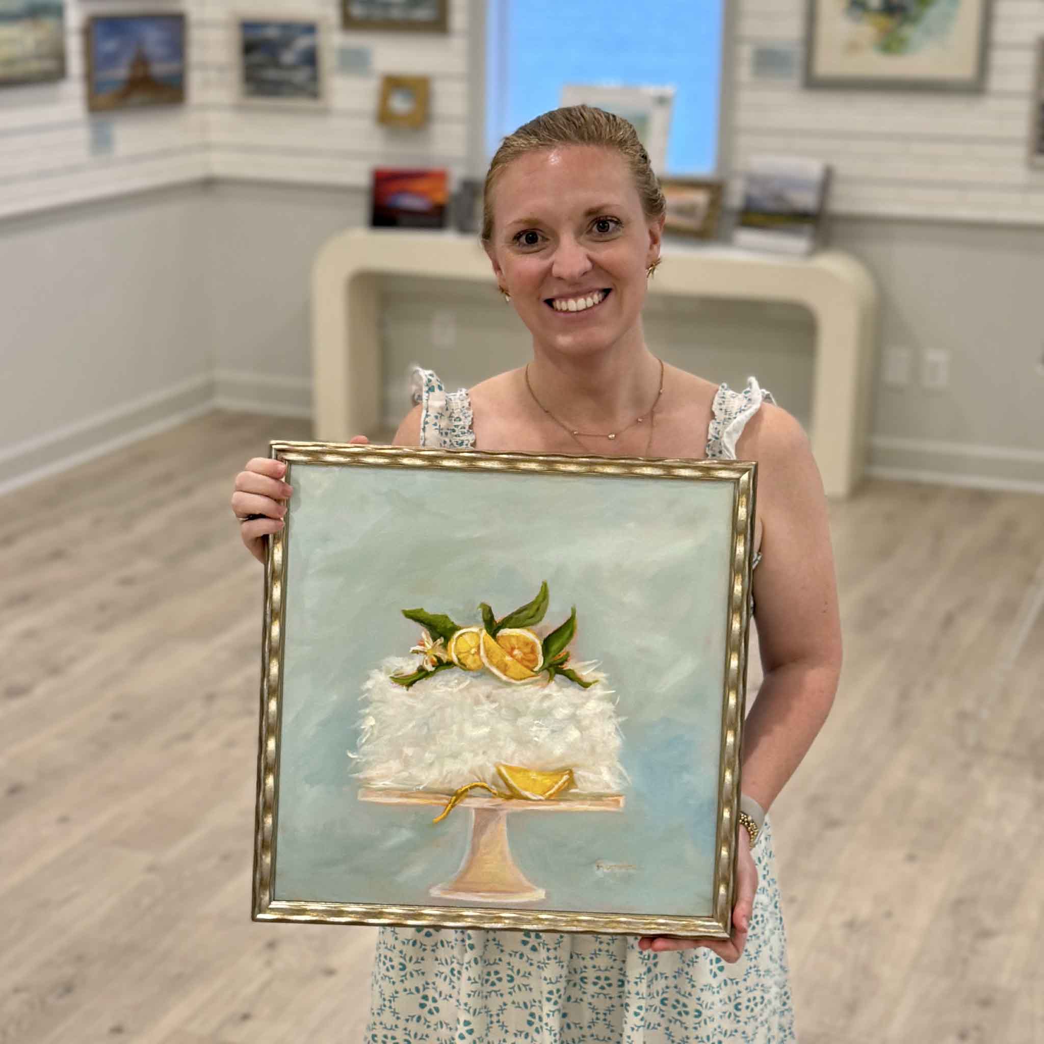 Local artist Jenny Reynolds holding Station 22 Coconut Cake (Secret Recipe!), an original square oil painting inspired by the famous Charleston dessert and framed in her signature champagne frame at Gray Man Gallery