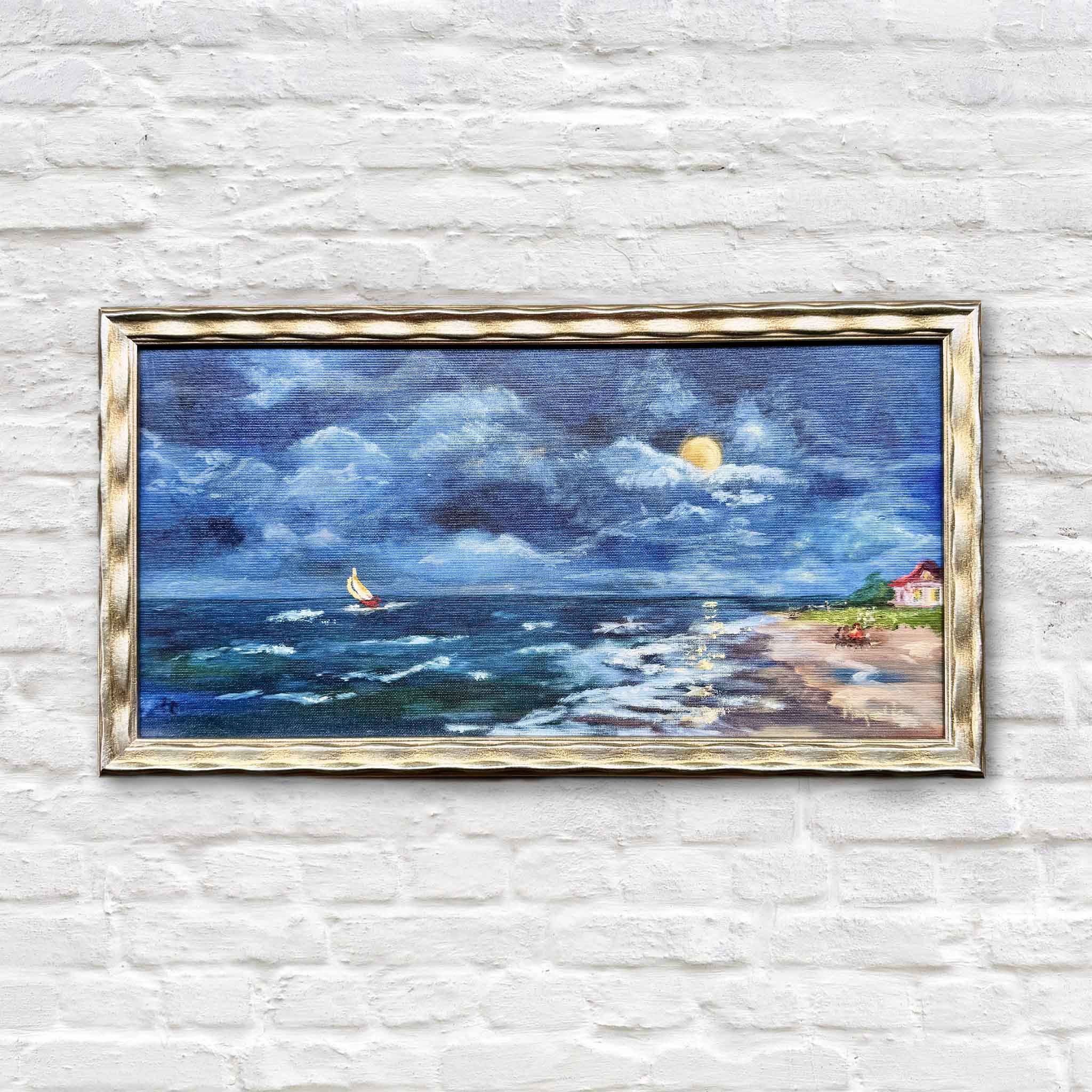 Summer Nights by local artist Jenny Reynolds is an original coastal oil painting featuring moonlit ocean waves, dramatic blue clouds, a sailboat on the horizon, and a glowing beach cottage, framed in the artist’s signature gold frame and available at Gray Man Gallery in Pawleys Island