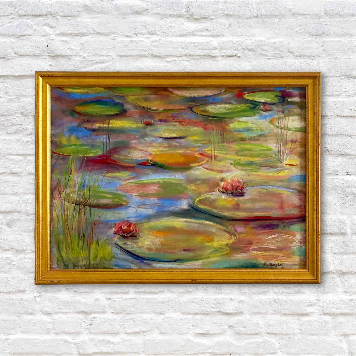 Brookgreen Beauty, an original pastel painting by local South Carolina artist Joanne Willoughby, depicting colorful lily pads, pink water lilies, and reflections in a pond at Brookgreen Gardens in Murrells Inlet. Expressive shades of green, turquoise, blue, gold, and pink fill the composition, presented in a classic gold frame against a white brick wall at Gray Man Gallery in Pawleys Island, South Carolina.
