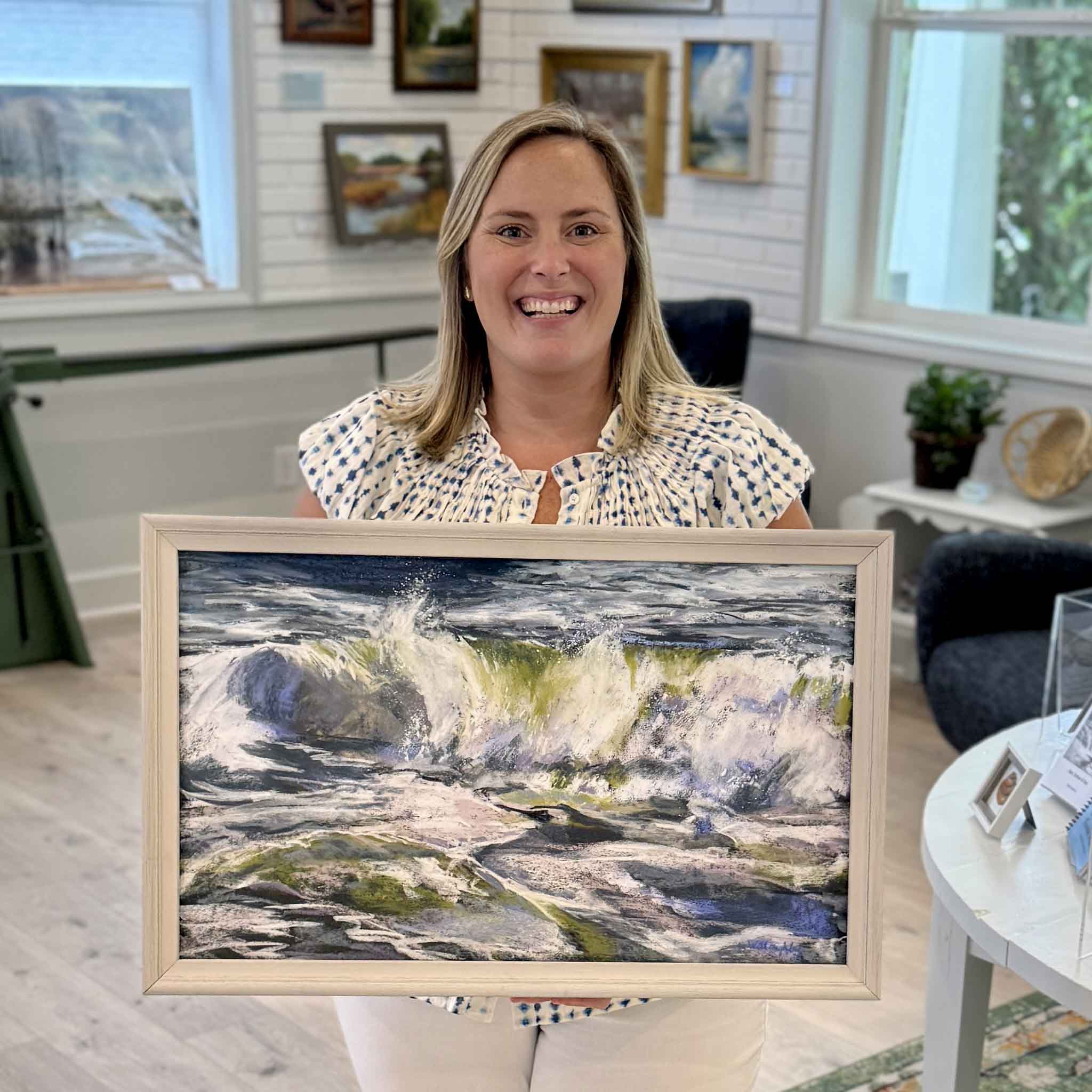 Bordy holding Frolic, an original pastel by local artist Joanne Willoughby at Gray Man Gallery, showing scale of the framed coastal wave artwork with rich texture and movement