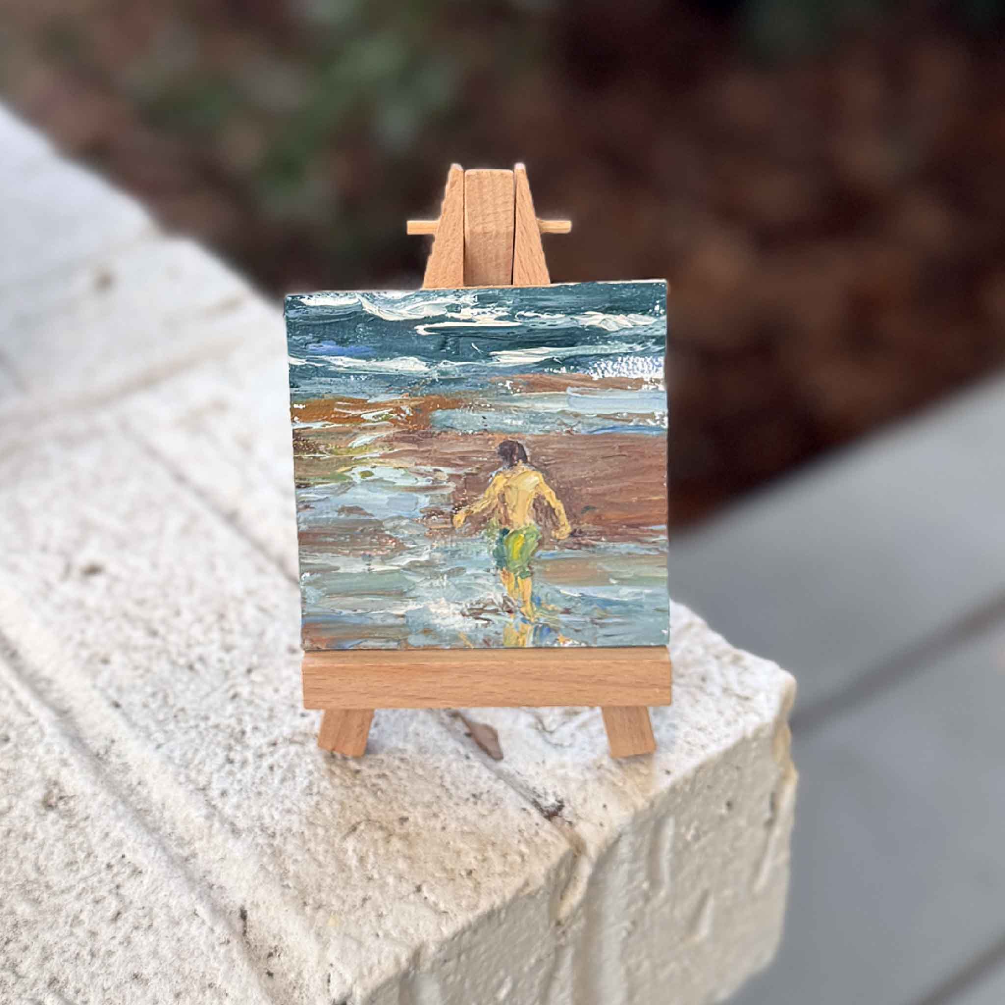 Small 3x3 original oil painting by Joanne Willoughby displayed on a wooden easel, featuring a boy exploring the beach with expressive, layered coastal brushstrokes.