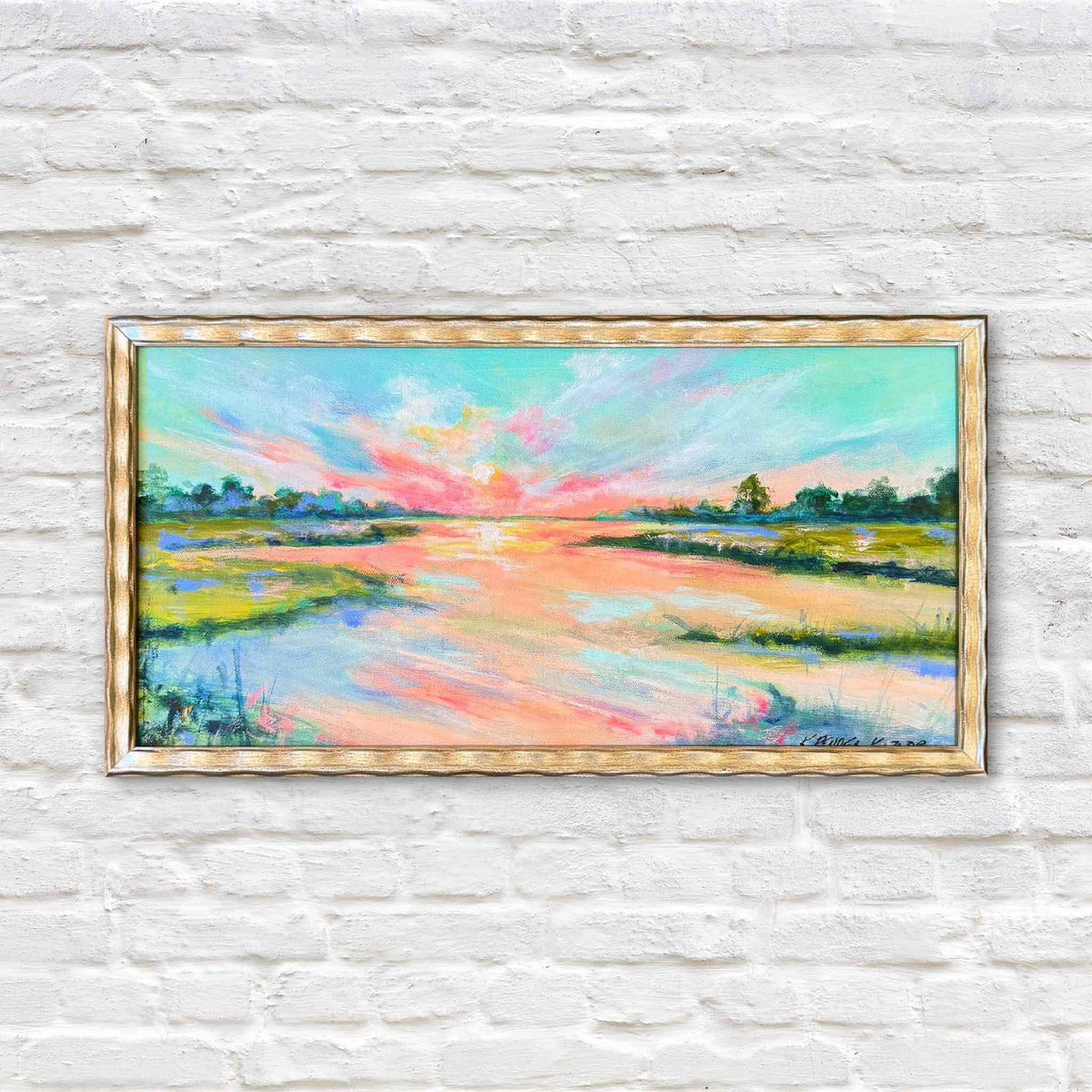The Last Blush, an original oil painting by South Carolina artist Kathleen Kazior, depicting a colorful Lowcountry marsh sunset with brilliant coral pink, turquoise blue, peach, and golden light reflecting across a winding tidal creek. Lush green marsh grasses and distant trees frame the luminous coastal landscape. Presented in a distressed metallic gold frame against the signature white brick wall at Gray Man Gallery in Pawleys Island, South Carolina.