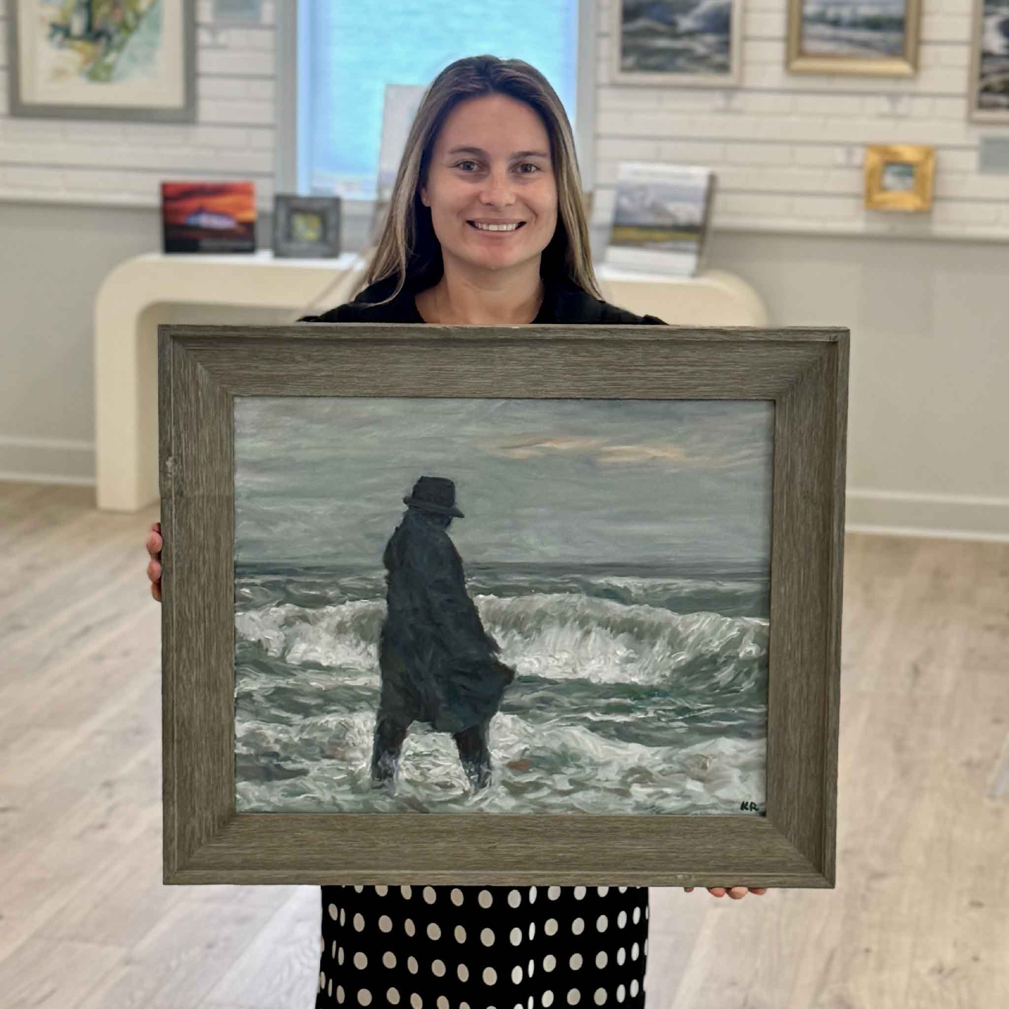 Kyra holding Gray Man II, an original oil painting by local artist Kathy Robinson depicting the legendary Gray Man of Pawleys Island standing in the surf. Framed coastal artwork available at Gray Man Gallery in Pawleys Island, South Carolina.