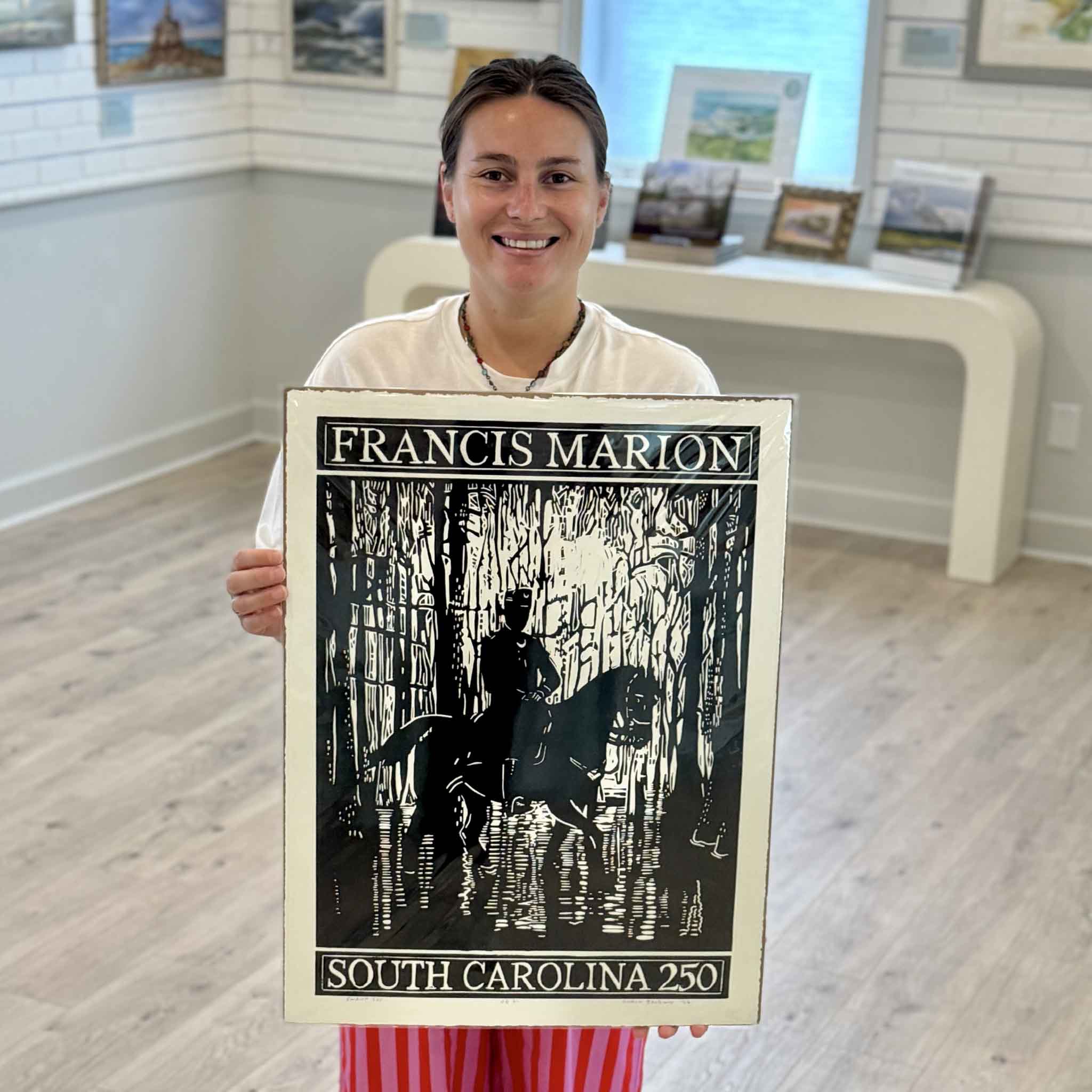 Kyra of Gray Man Gallery holding Francis Marion: America 250, an original linocut by Aaron Baldwin commemorating the 250th anniversary of American independence.