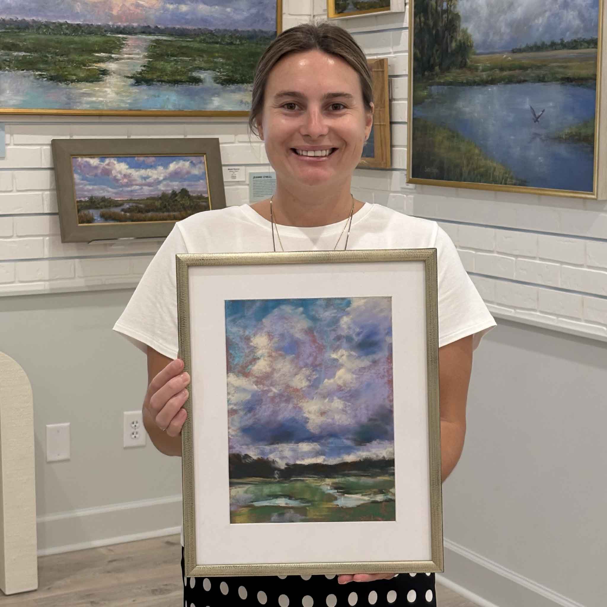Kyra holding After the Rain by Joanne Willoughby at Gray Man Gallery in Pawleys Island, South Carolina. This original Lowcountry pastel landscape is professionally matted, custom framed, and protected with premium Water White glass, showcasing the artist's expressive sky and tranquil marsh scene.