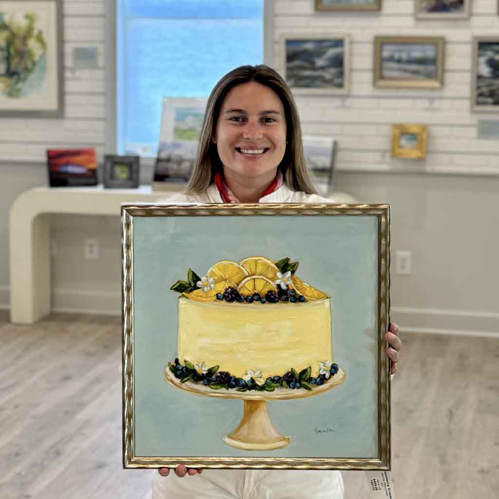 Kyra holding Blueberry Cream, an original oil painting by Jenny Reynolds from the Southern Sweets Collection featuring a decorated blueberry and lemon cake in a gold frame at Gray Man Gallery.