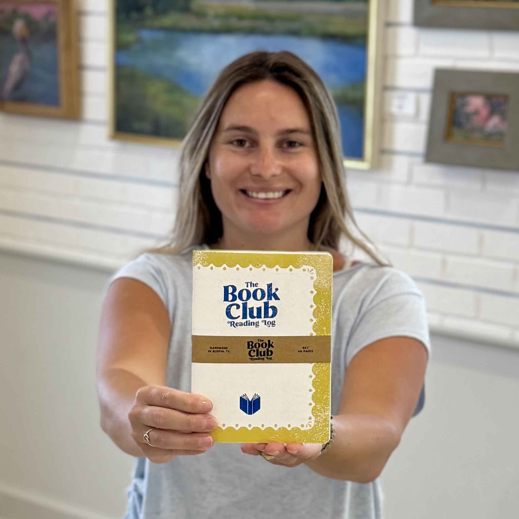 Kyra holding The Book Club Reading Log Book by Justin Ryan Books at Gray Man Gallery in Pawleys Island, SC. This 5x7 reading journal is designed for book clubs and avid readers to record books read, authors, ratings, favorite quotes, discussion topics, and reading notes. Hand-assembled in Austin, Texas.
