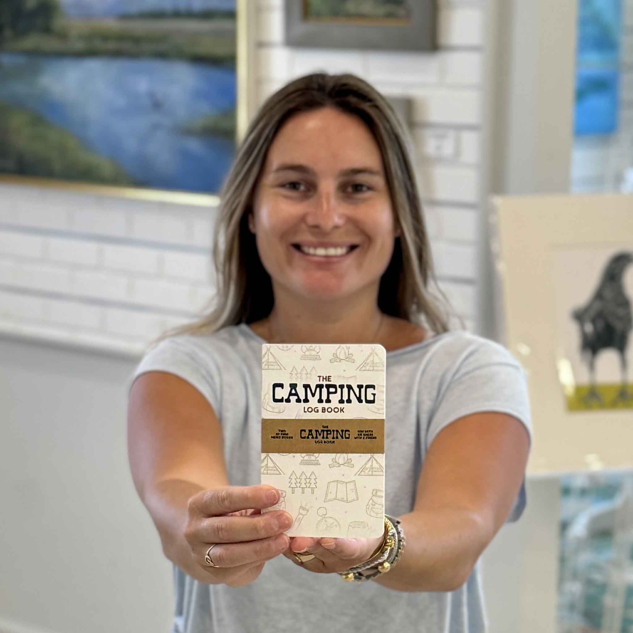 Kyra holding The Camping Log Book by Justin Ryan Books at Gray Man Gallery in Pawleys Island, South Carolina. This pocket-sized camping journal helps campers record campgrounds, trip dates, weather conditions, campsites, memorable adventures, wildlife sightings, gear notes, and travel memories. Designed, printed, and hand-assembled in Austin, Texas.