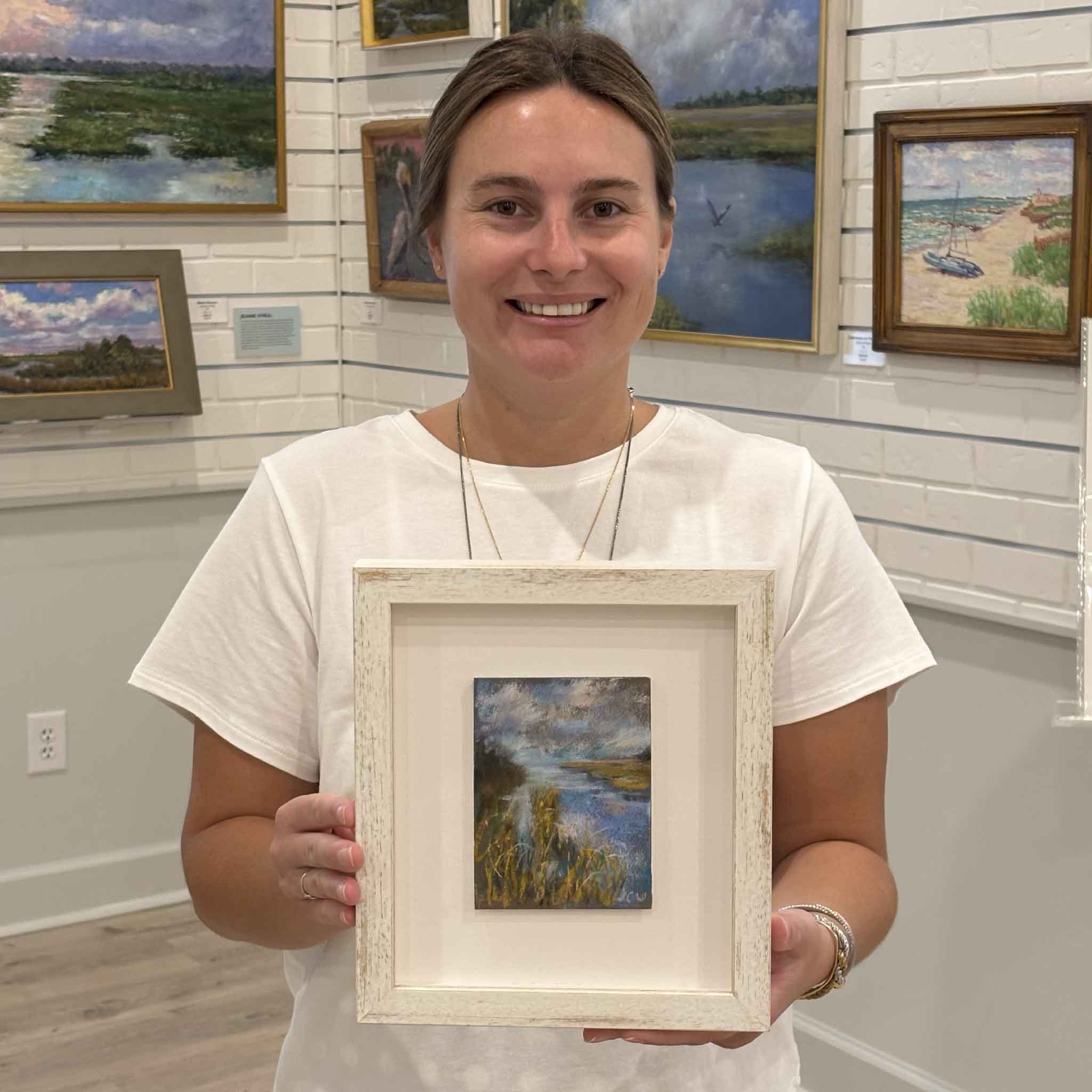 Kyra holds Chance of Rain, an original pastel marsh landscape by Lowcountry artist Joanne Willoughby, at Gray Man Gallery in Pawleys Island, South Carolina. Professionally matted and custom framed with premium Water White glass, this original artwork features a winding tidal creek, luminous skies, and the tranquil coastal scenery that defines the South Carolina Lowcountry.
