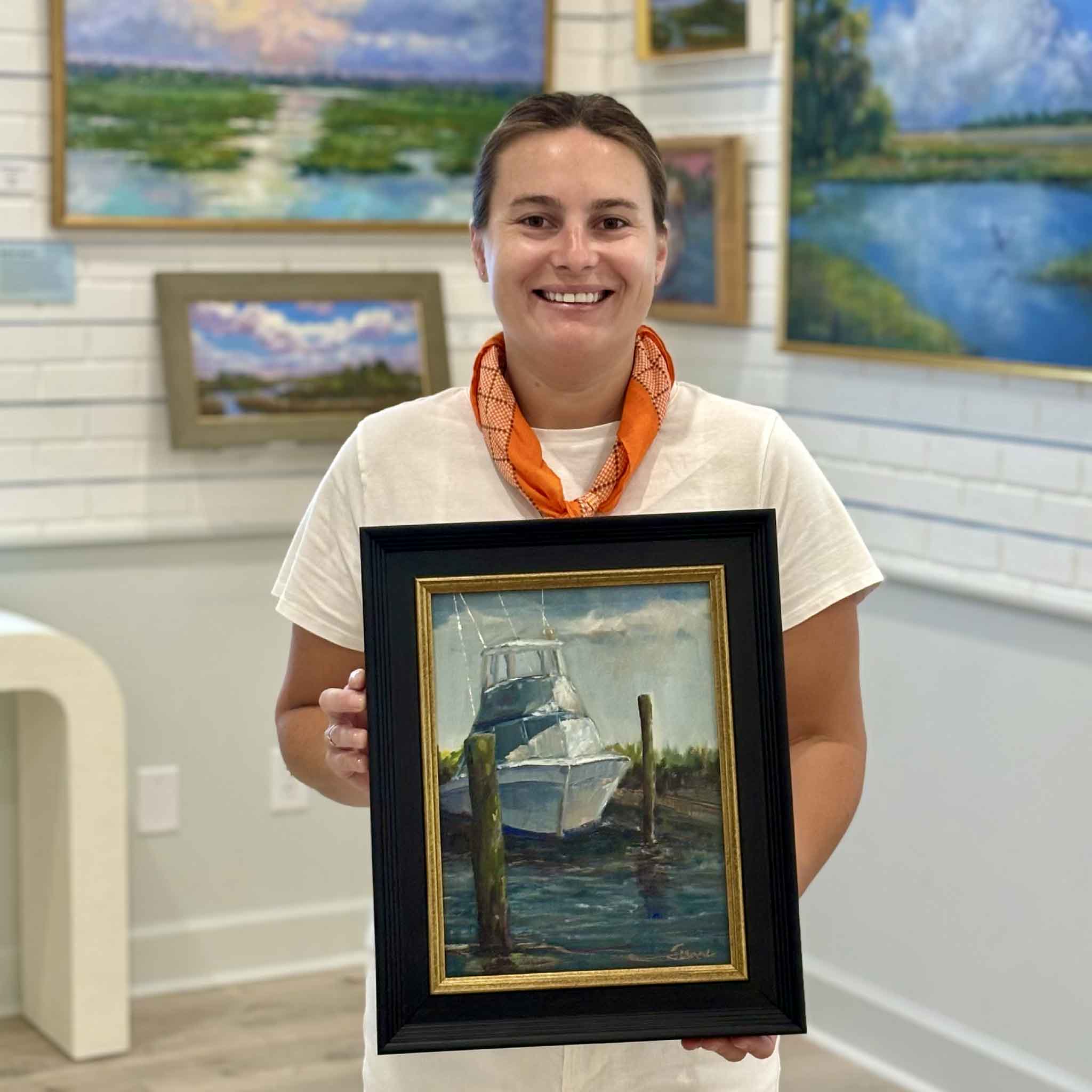 Gray Man Gallery team member Kyra holding Docked for the Day by Jeanne O'Neal to show scale, an original Georgetown harbor oil painting featuring a sportfishing boat moored at the dock in coastal South Carolina.