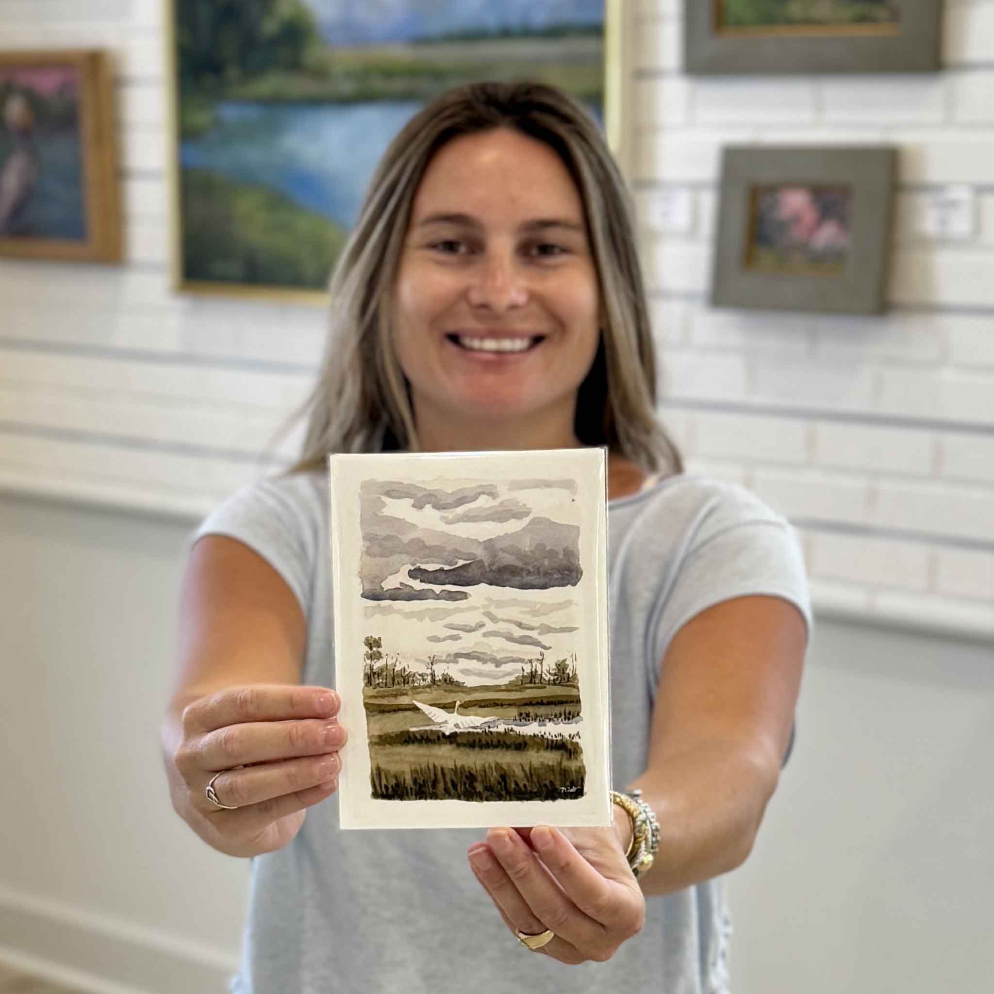 Kyra holding Heron Taking Flight, a 5x7 print by local artist Maggie Pelton. This Lowcountry marsh and heron artwork fits standard 5x7 frames and is available at Gray Man Gallery in Pawleys Island, South Carolina.