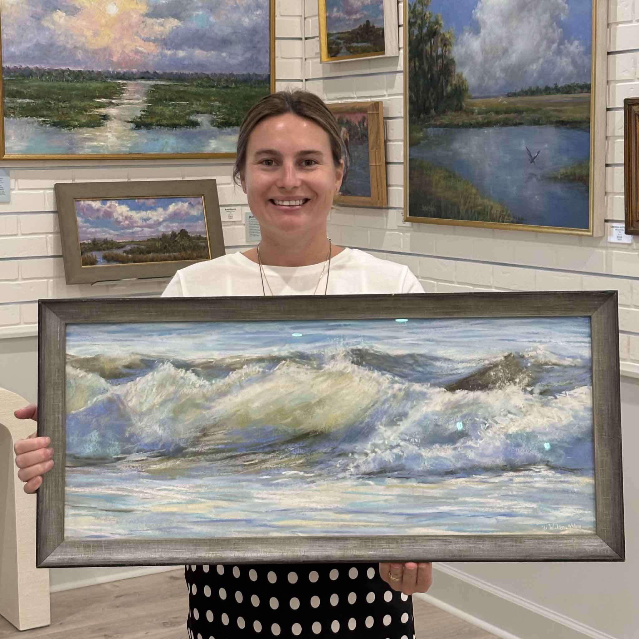Kyra holds A Light Breeze, an original soft pastel by Joanne Willoughby featuring rolling Atlantic Ocean waves, professionally framed with museum glass and available at Gray Man Gallery in Pawleys Island, South Carolina.