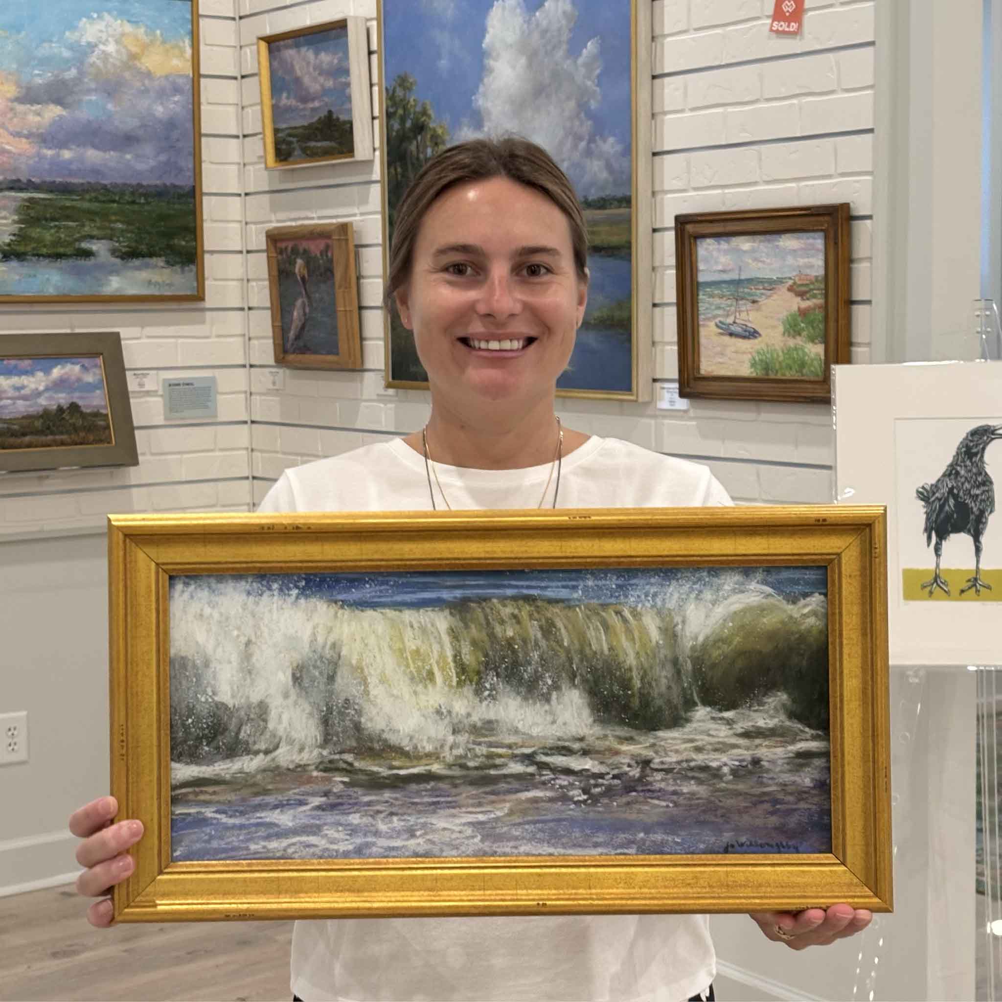 Kyra holds Crescendo, an original ocean pastel painting by local artist Joanne Willoughby featuring a dramatic breaking Atlantic wave, professionally framed with museum glass and available at Gray Man Gallery in Pawleys Island, South Carolina.
