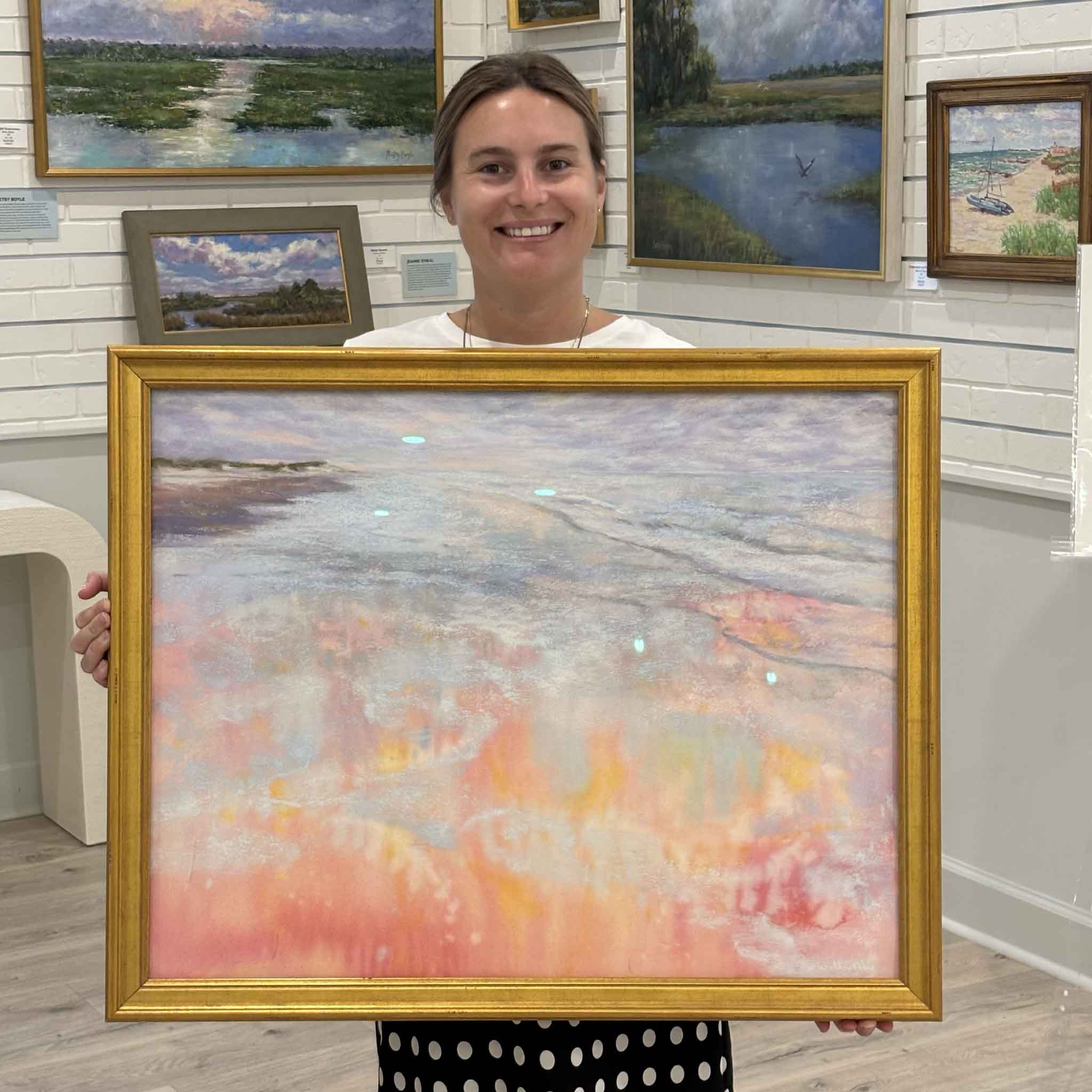 Kyra holds Pawleys Magic, an original soft pastel by Joanne Willoughby inspired by the glowing colors and reflections of a Pawleys Island sunset, at Gray Man Gallery in Pawleys Island, South Carolina.