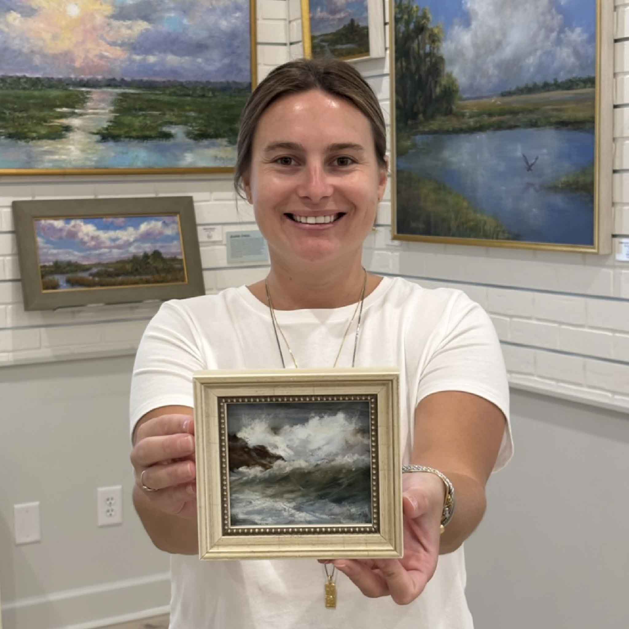 Kyra holds Splash, an original ocean wave pastel painting by local artist Joanne Willoughby, professionally framed with Water White glass and available at Gray Man Gallery in Pawleys Island, South Carolina.