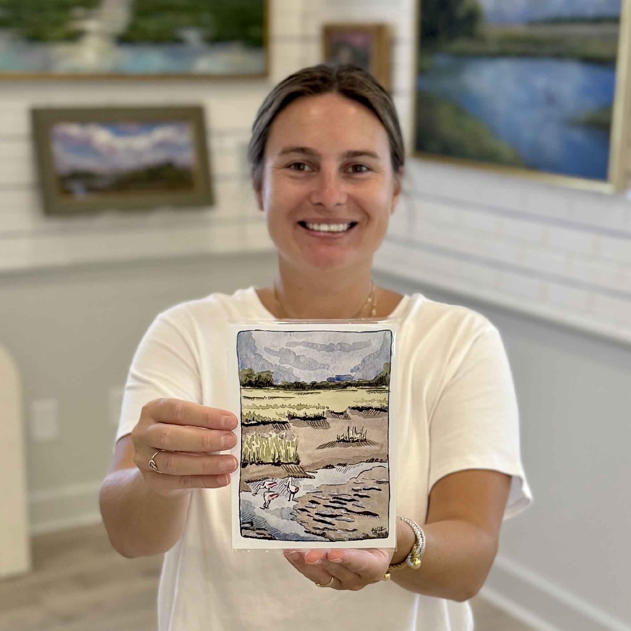 Kyra holds Maggie Pelton's Following the Tide 5x7 archival giclée print at Gray Man Gallery in Pawleys Island, South Carolina, showcasing the Roseate Spoonbill watercolor reproduced on museum-quality fine art paper.