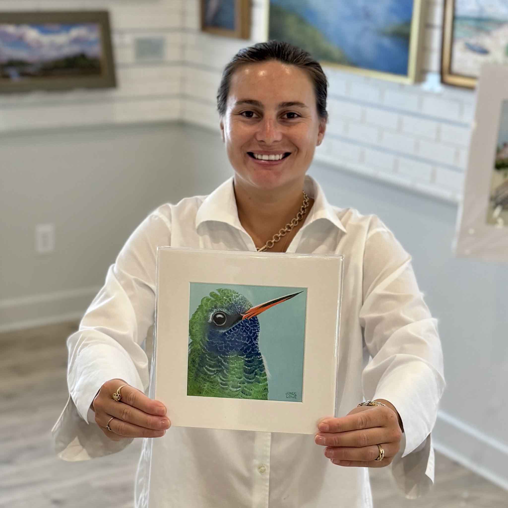 Kyra holds Broad-billed Hummingbird II by local artist Nancy Jones Lowe at Gray Man Gallery in Pawleys Island, South Carolina. This colorful hummingbird print is professionally printed on 100% cotton archival paper and matted to fit a standard 8x8 frame, making it easy to display in any ready-made frame.