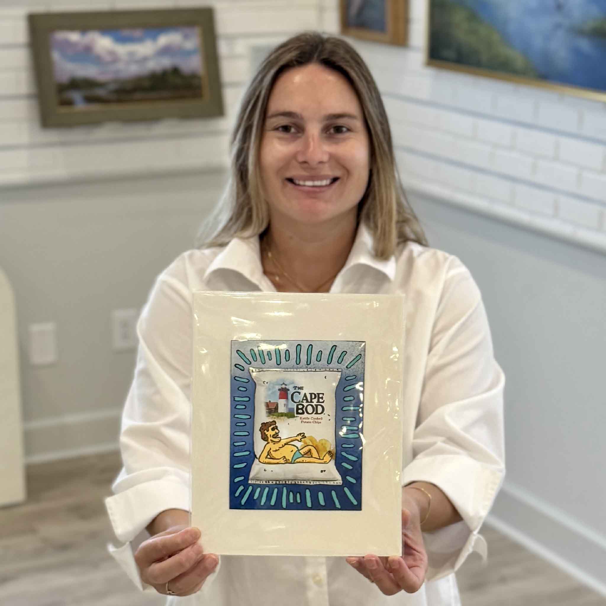 Kyra holds Cape Bod Blue by Charleston artist Nick Kawczynski at Gray Man Gallery in Pawleys Island, South Carolina. This original mixed media artwork transforms a reclaimed Cape Cod potato chip box into playful coastal art and is professionally matted to fit a standard 8x10 frame.