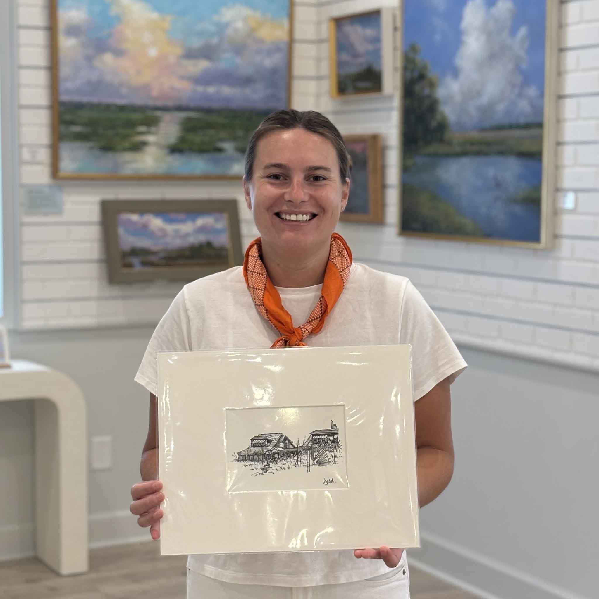 Kyra holding Pawleys Island Beach Houses by Todd Halamka at Gray Man Gallery in Pawleys Island, South Carolina. This professionally matted pen-and-ink print captures the timeless appeal of classic Pawleys Island beach houses and fits a standard 11x14 frame for easy display without custom framing.

