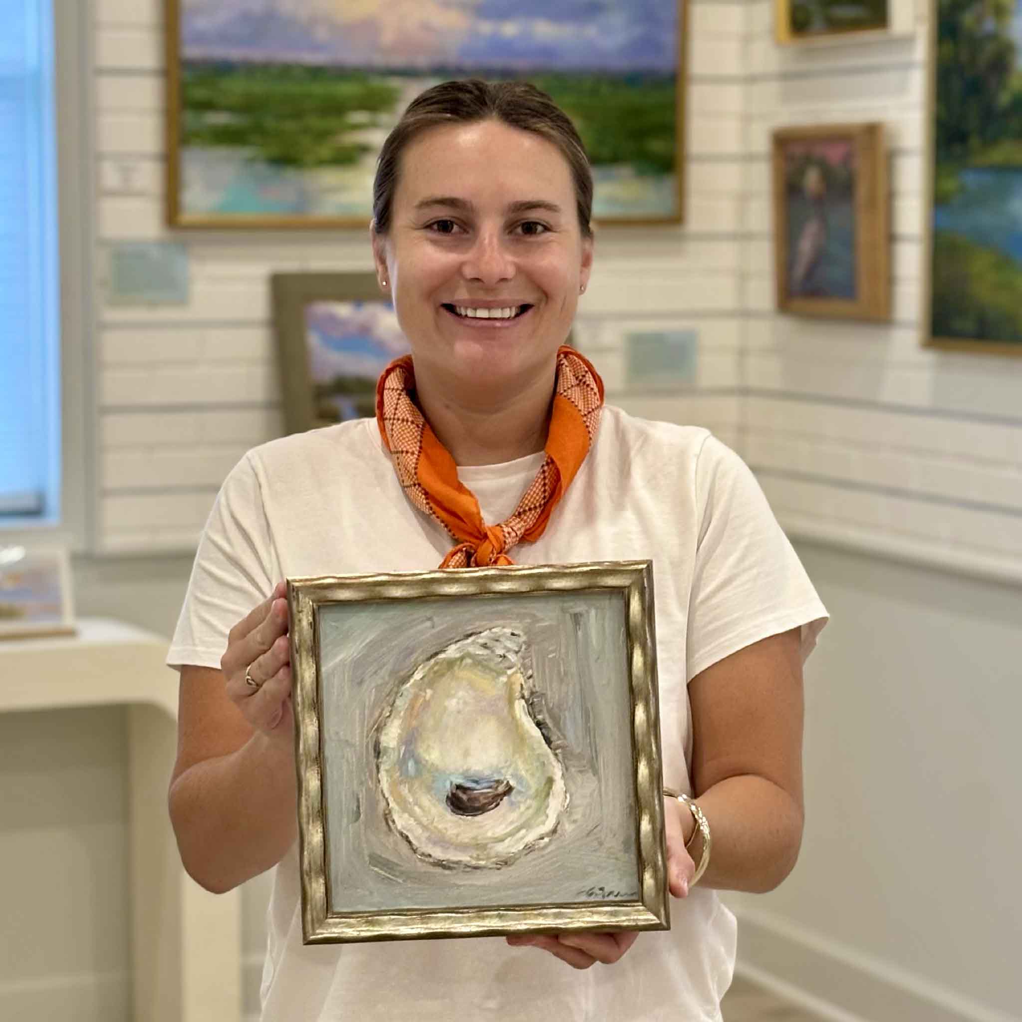 Kyra holding Radiance by local South Carolina artist Allison Farr to show scale, an original framed oyster shell oil painting from the Lowcountry Jewels collection at Gray Man Gallery in Pawleys Island, South Carolina.