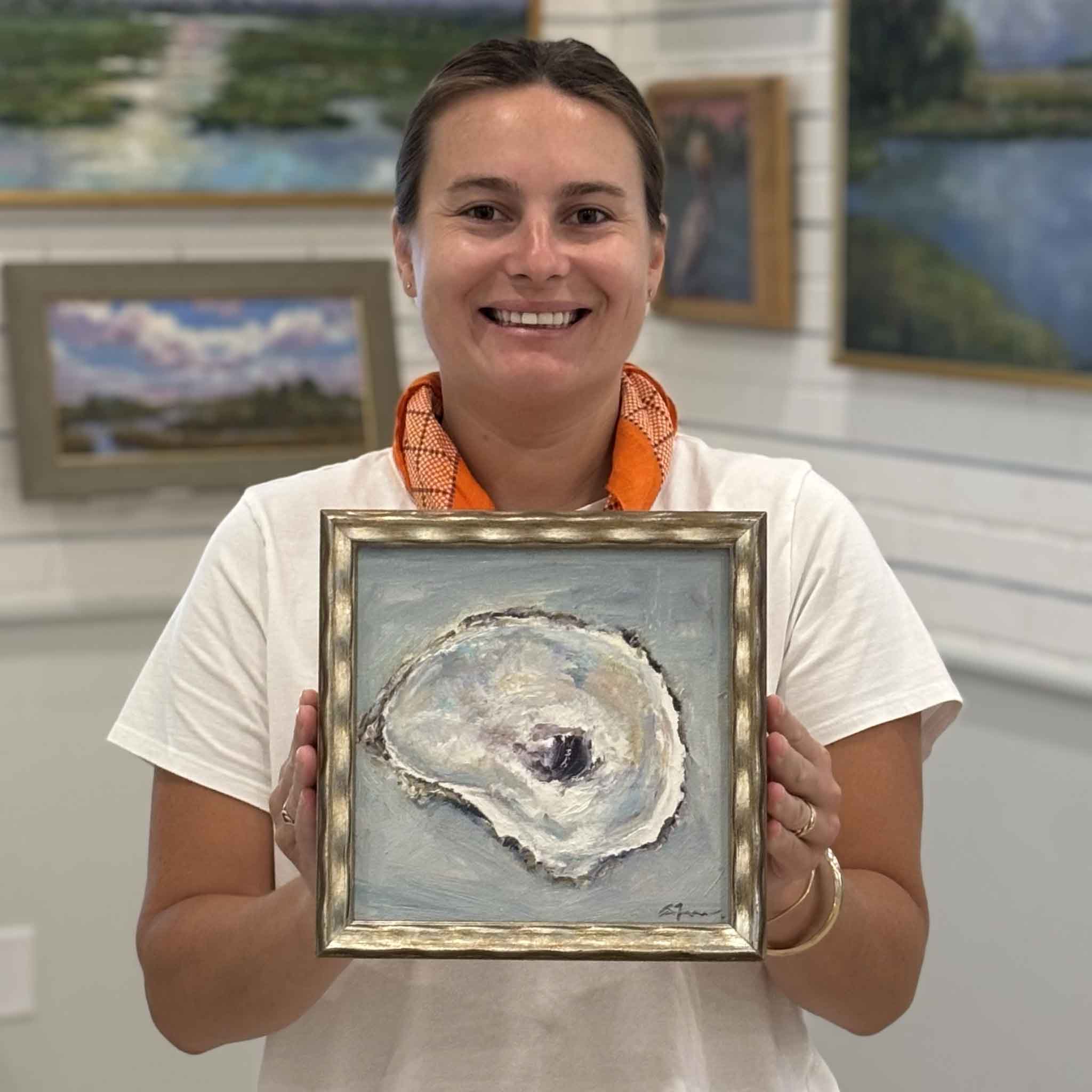 Kyra holding Reflection by local South Carolina artist Allison Farr to show scale, an original framed oyster shell oil painting from the Lowcountry Jewels collection at Gray Man Gallery in Pawleys Island, South Carolina.