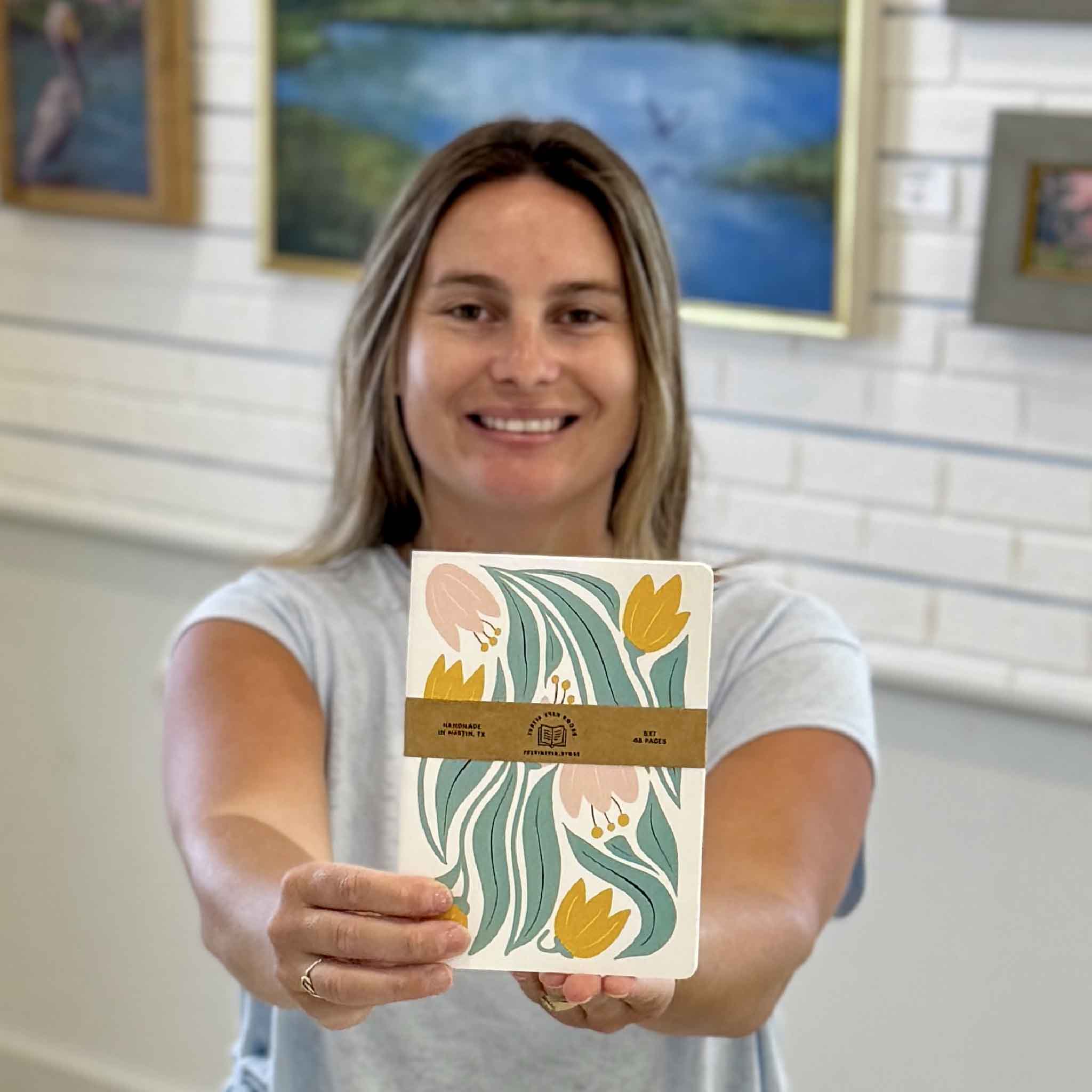 Kyra holding the Tulip Floral Notebook by Justin Ryan Books at Gray Man Gallery in Pawleys Island, South Carolina. This 5x7 blank notebook features a colorful tulip design and is designed, printed, and hand-assembled in Austin, Texas.