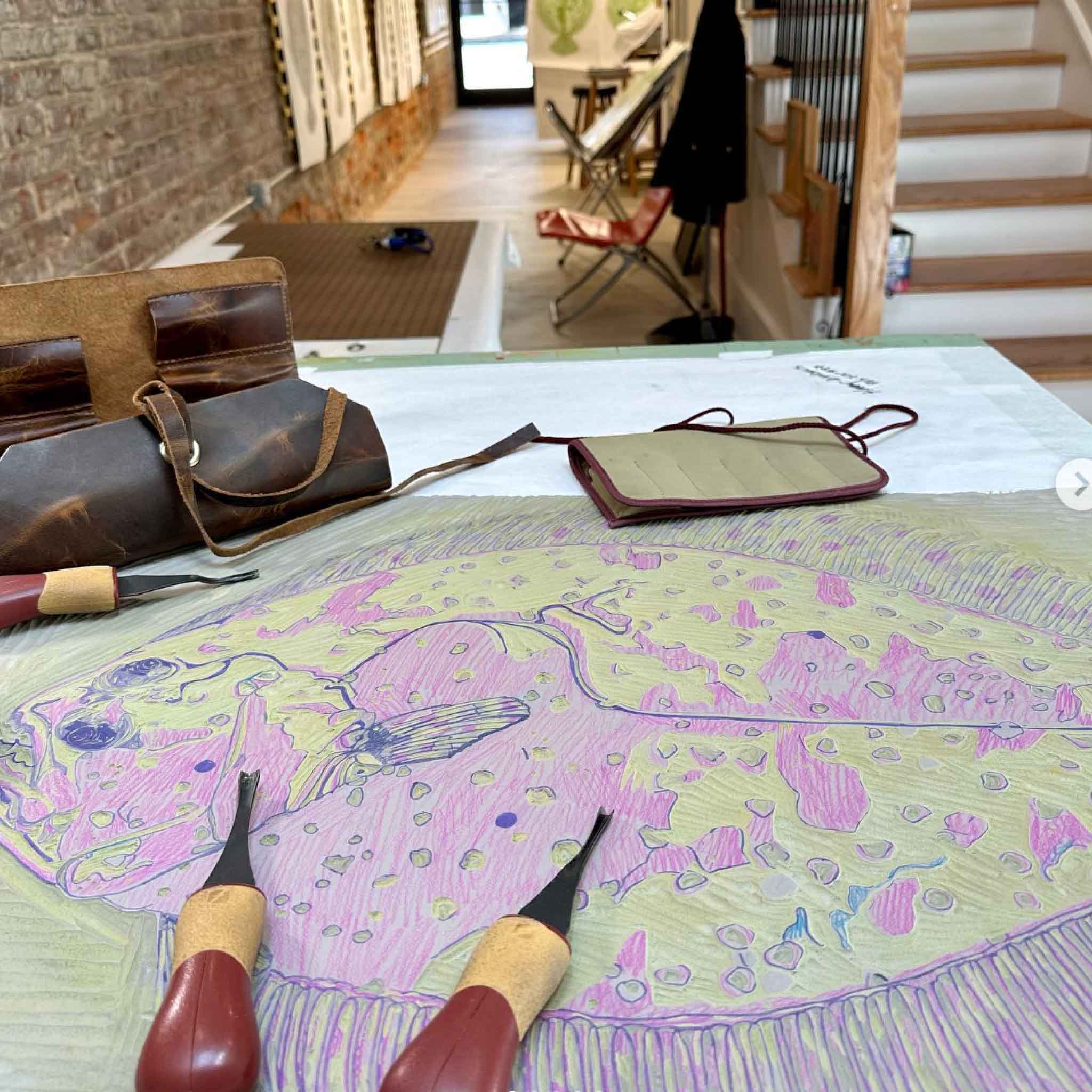 Work-in-progress photo of Laurie McIntosh's Flat Fred reduction linocut, showing the hand-carved linoleum block and carving tools in the artist's South Carolina studio. This behind-the-scenes image highlights the intricate reduction printmaking process used to create the original Flat Fred artwork available at Gray Man Gallery in Pawleys Island, South Carolina.