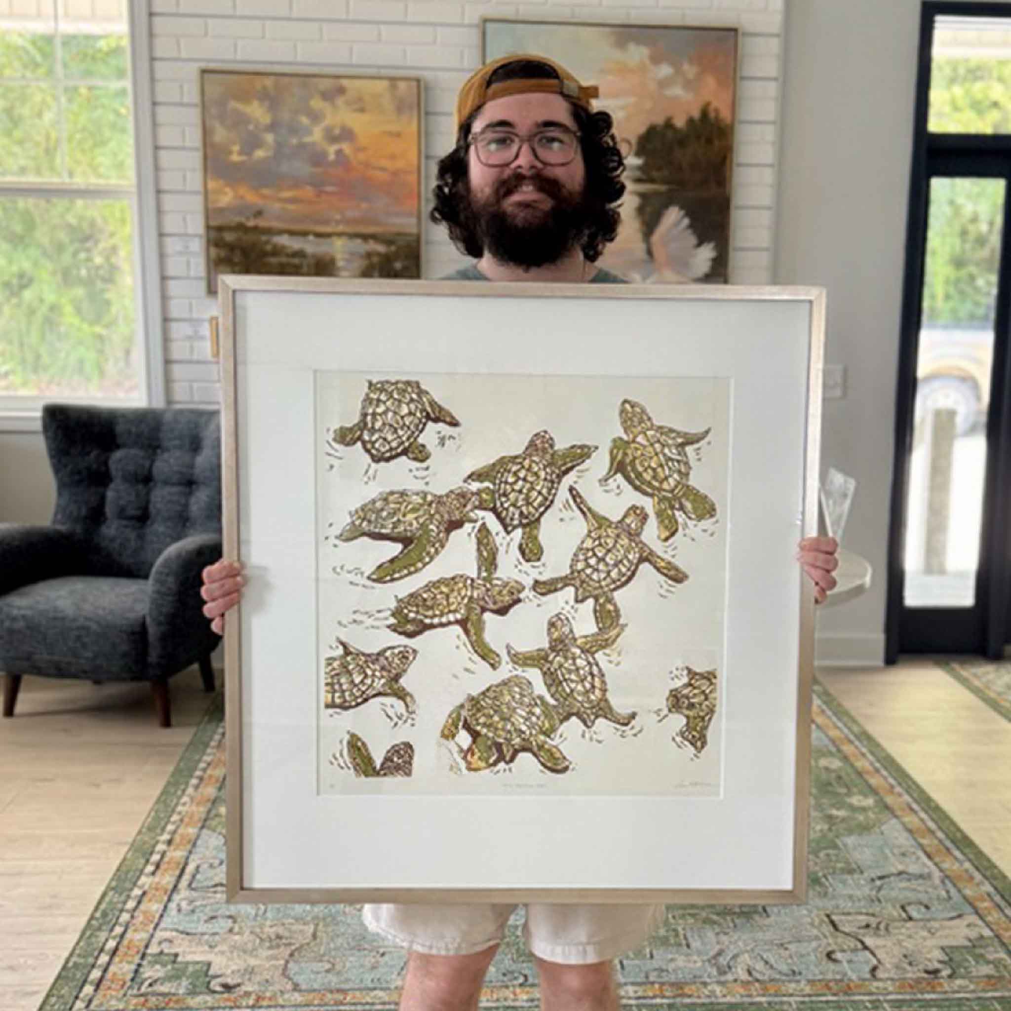Framed Let’s Follow Her original reduction linocut by Laurie McIntosh held inside Gray Man Gallery in Pawleys Island, showing the large-scale sea turtle artwork professionally matted and finished in the artist’s signature champagne frame.