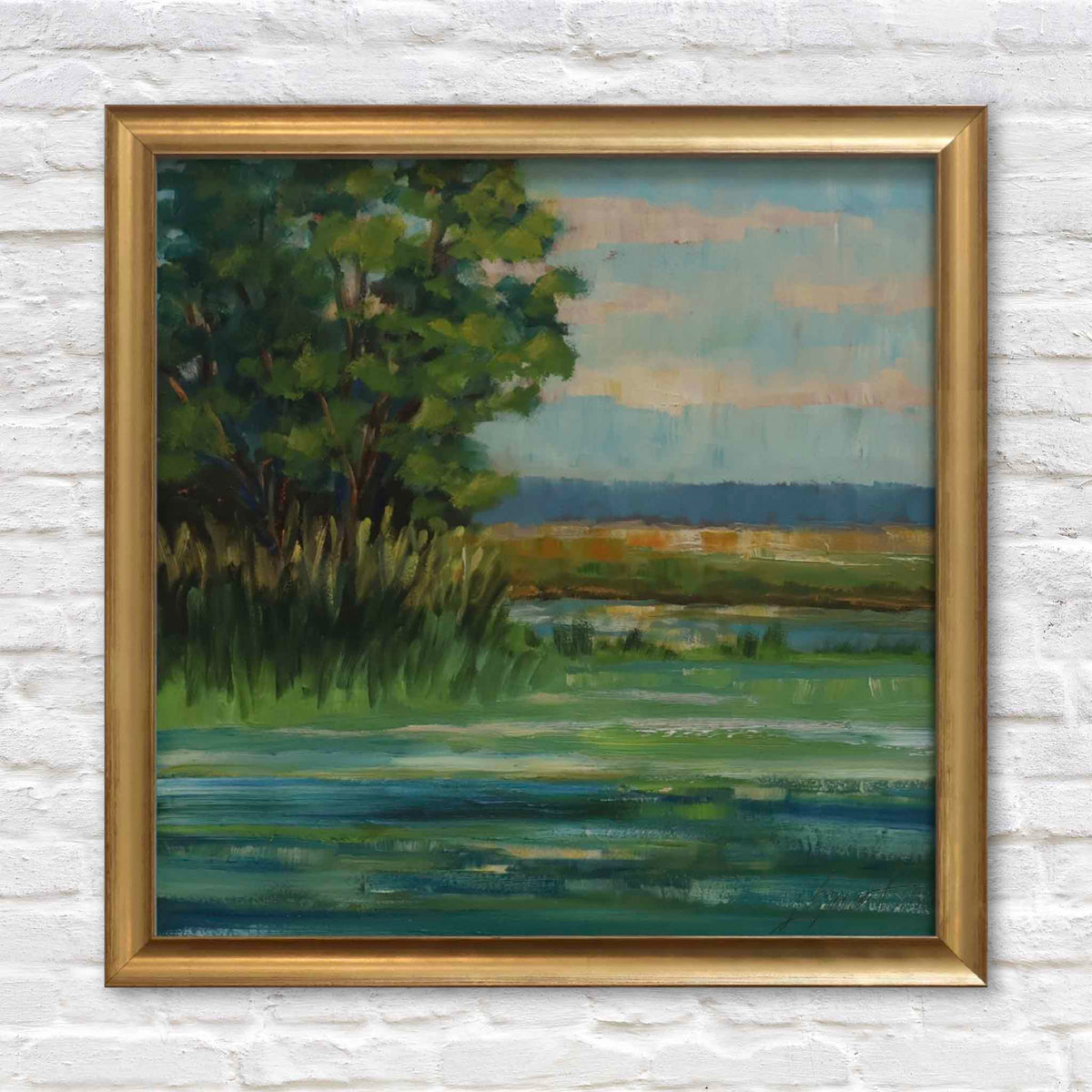 Coastal Tides, an original oil landscape painting by local South Carolina artist Libby Smart, featuring a peaceful Lowcountry tidal marsh with leafy green trees, tall coastal grasses, winding blue-green waterways, distant golden marshlands, and a softly clouded sky. Presented in a classic gold frame against a white brick wall at Gray Man Gallery in Pawleys Island, South Carolina.