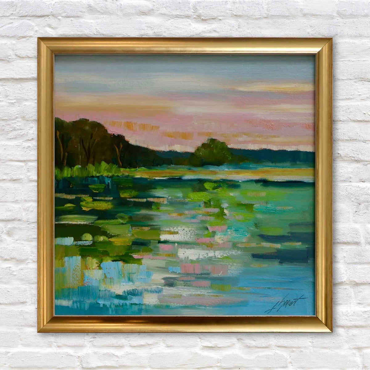 Glistening Water, an original oil painting by local South Carolina artist Libby Smart, depicting a tranquil Lowcountry waterway with shimmering turquoise and emerald reflections, floating green vegetation, a distant tree line, and a glowing pink, peach, and golden evening sky. Beautifully presented in a classic gold frame against a white brick wall at Gray Man Gallery in Pawleys Island, South Carolina.