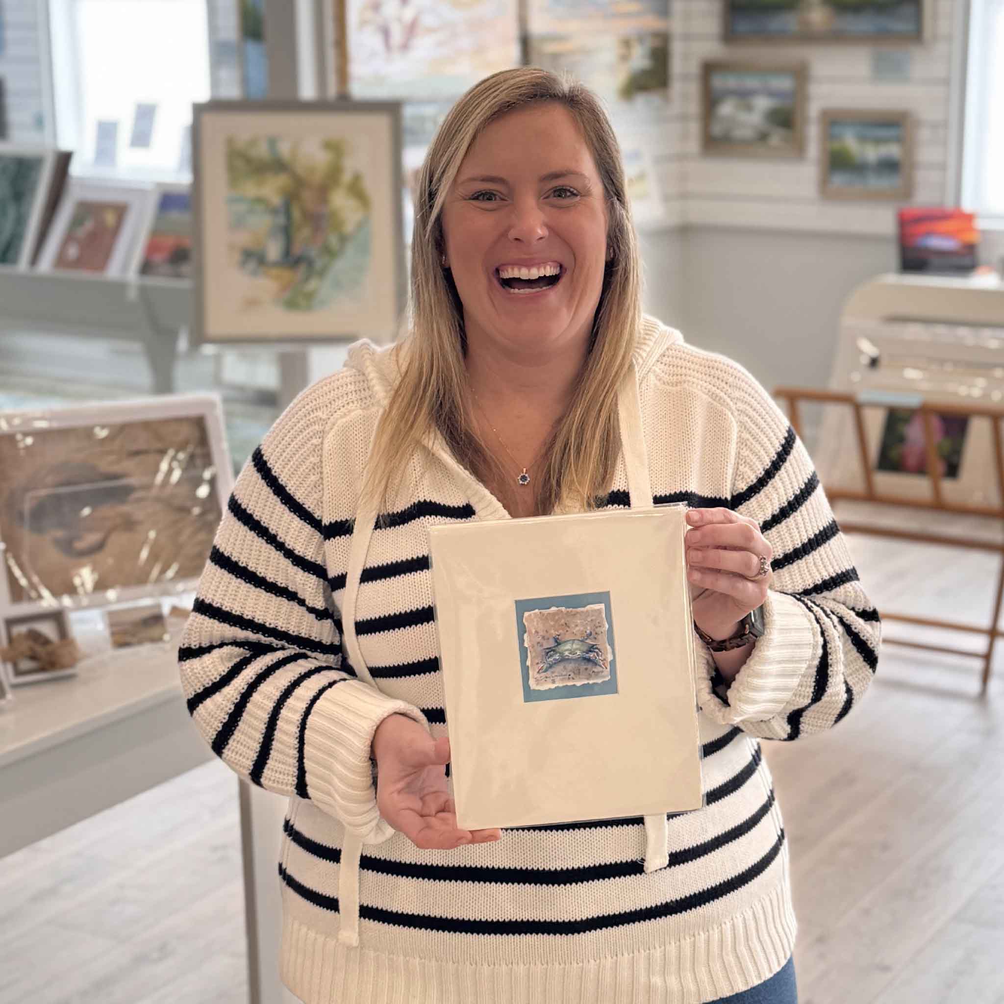 Team member holding Little Crab original watercolor by local artist Susan Schuhmacher inside Gray Man Gallery, showing scale and presentation.