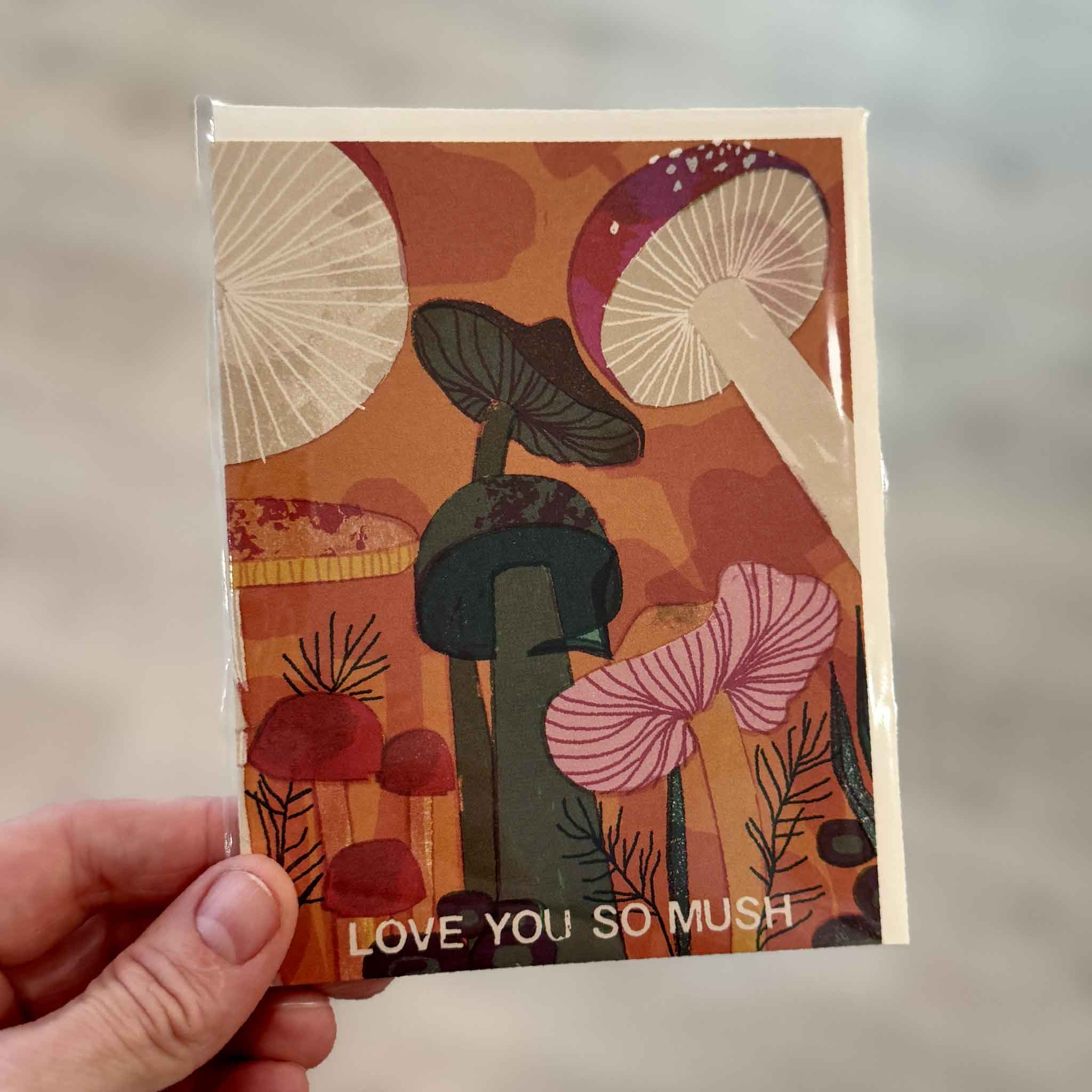 Love You So Mush greeting card illustrated by Barbara Dziadosz for Red Cap Cards, photographed inside Gray Man Gallery in Pawleys Island, South Carolina. The whimsical card features colorful illustrated mushrooms with the playful message "Love You So Mush."