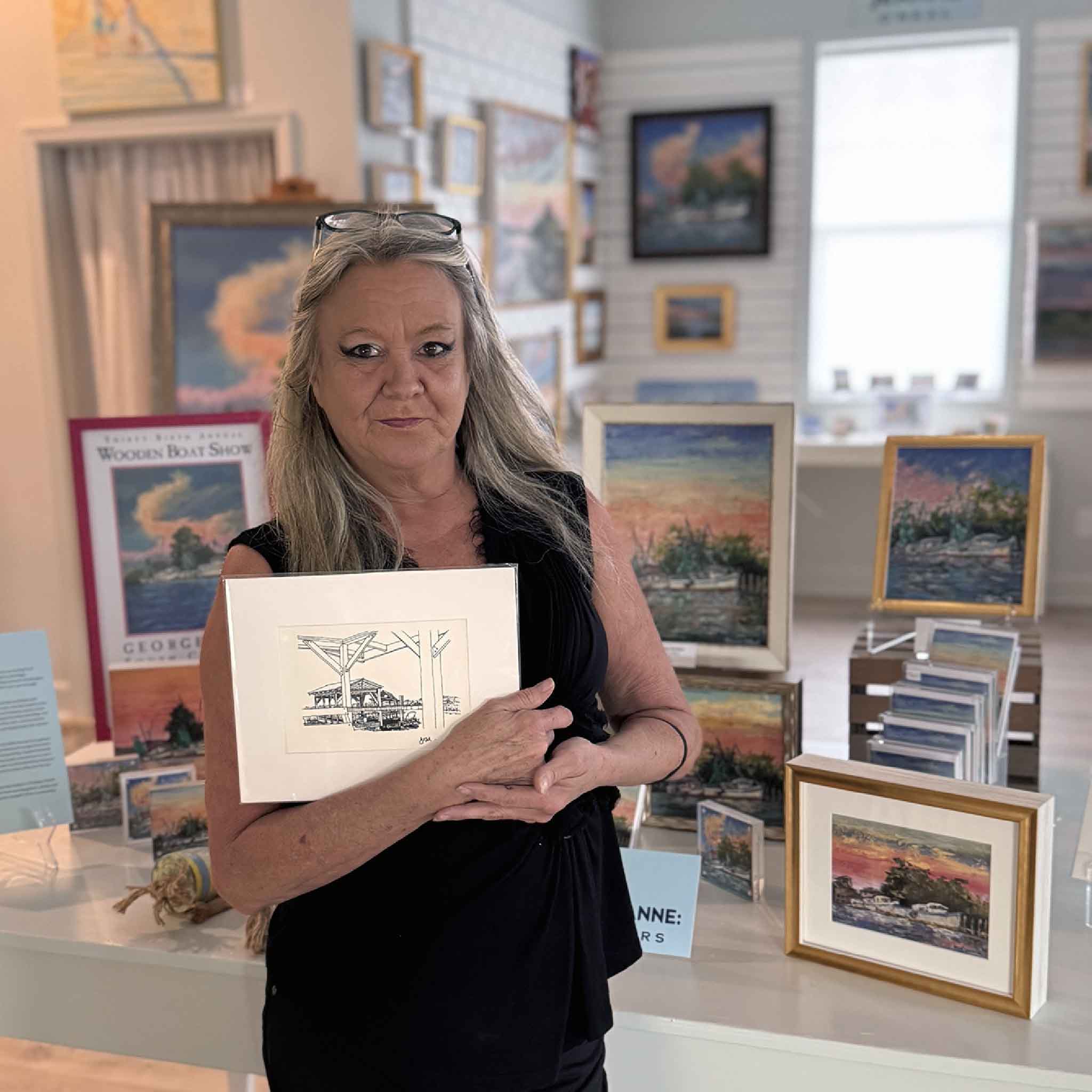 Gallery staff member holding Todd Halamka’s matted Marsh Dock sketch inside Gray Man Gallery, surrounded by coastal artwork.”