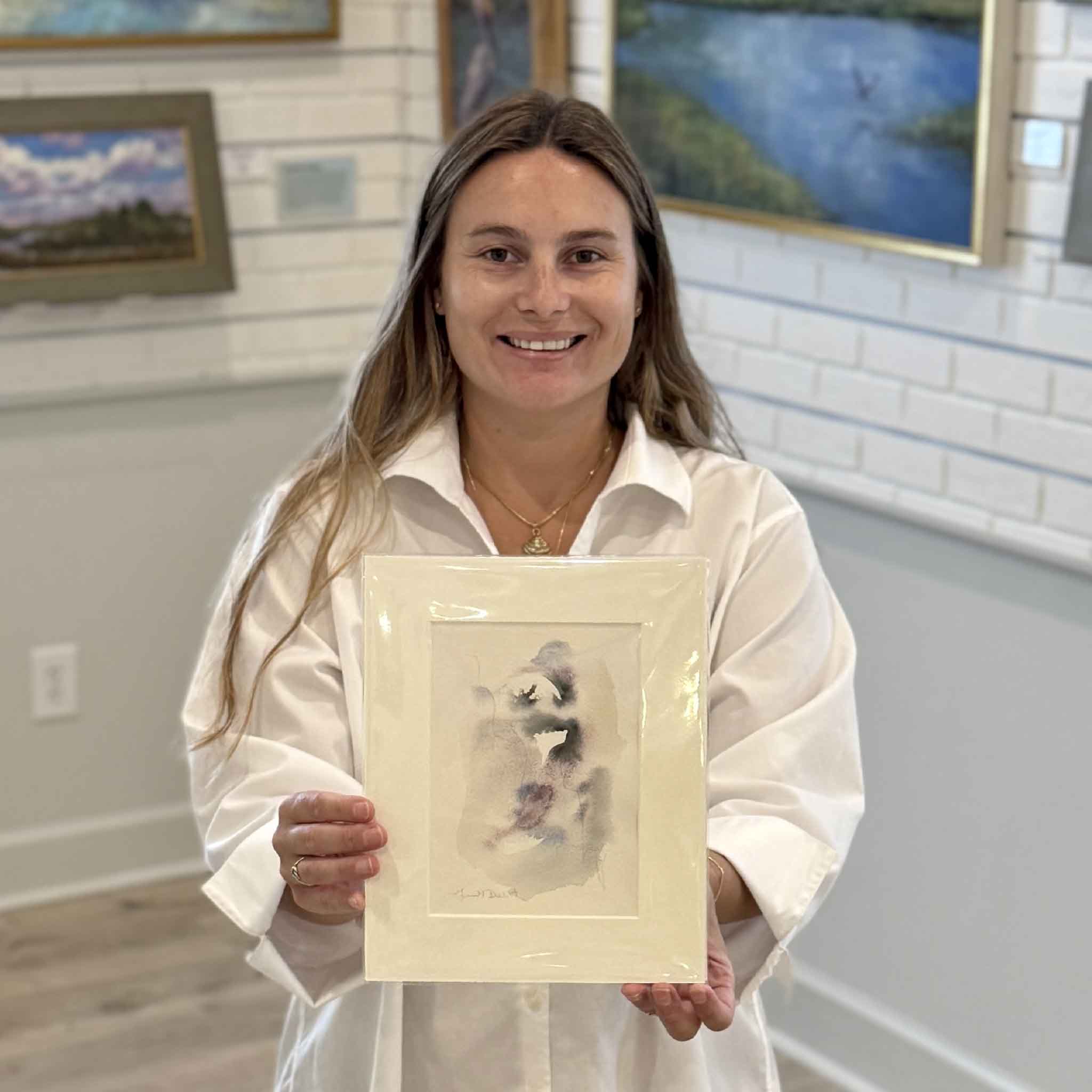 Kyra holds Tidal Study I, an original oyster-inspired watercolor by Lowcountry artist Megan DuMont. This one-of-a-kind artwork features soft abstract washes of gray, lavender, blue, and blush inspired by South Carolina oyster shells and tidal movement. Professionally matted to fit a standard 8x10 frame and available at Gray Man Gallery in Pawleys Island, SC.