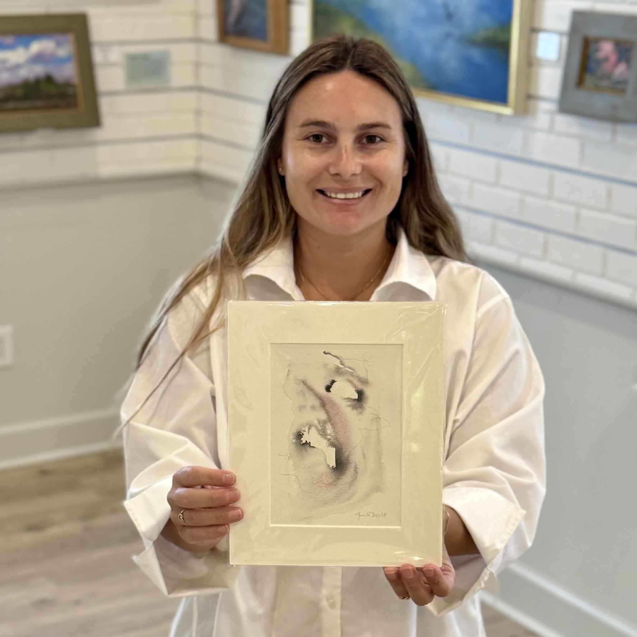 Kyra holds Tidal Study II, an original oyster-inspired watercolor by Lowcountry artist Megan DuMont. This one-of-a-kind abstract painting features soft coastal tones and flowing organic forms inspired by South Carolina oyster shells and tidal landscapes. Professionally matted to fit a standard 8x10 frame and available at Gray Man Gallery in Pawleys Island, SC.