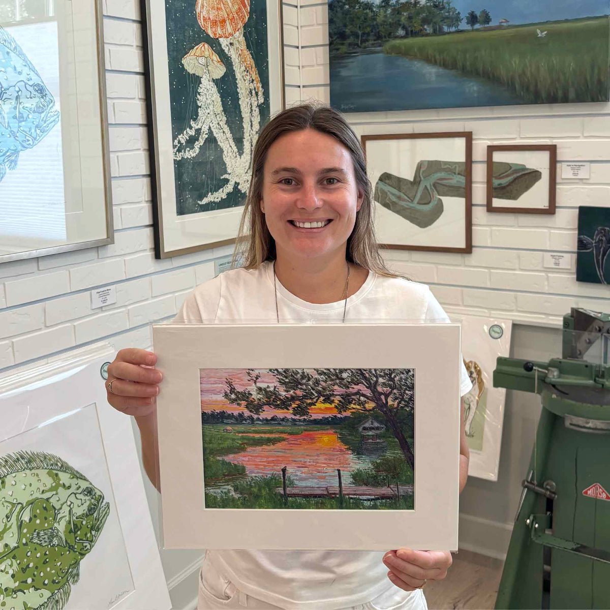 Kyra holds the 11×14 matted Fading Light giclée print by Michael Rogan at Gray Man Gallery in Pawleys Island, South Carolina, featuring Rogan’s Lowcountry marsh sunset painted in South Litchfield.