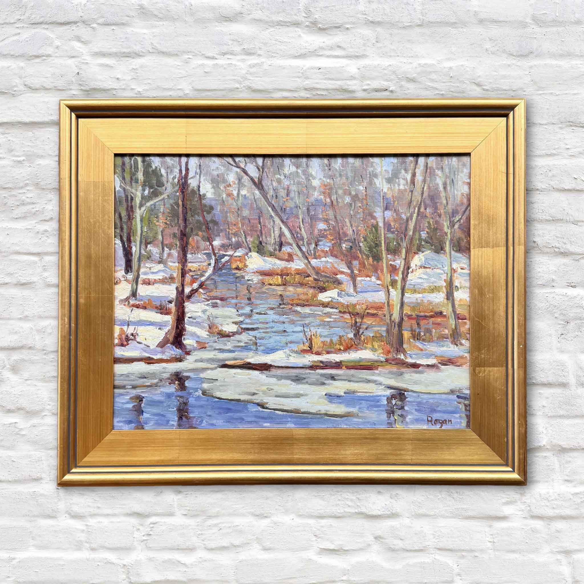 Framed original oil painting of a snowy creek and winter trees by artist Michael Rogan, displayed against a white brick wall at Gray Man Gallery.