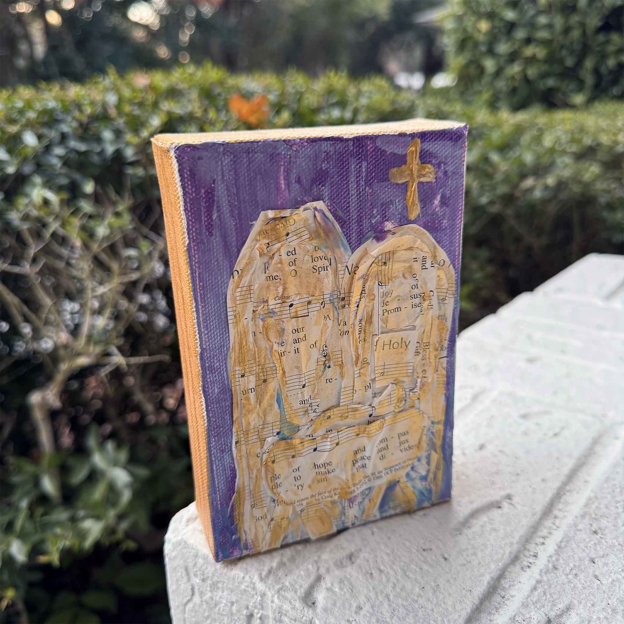 angled view of Jeanne O’Neal’s mixed-media Christmas artwork with hymn pages and gold accents on a purple canvas