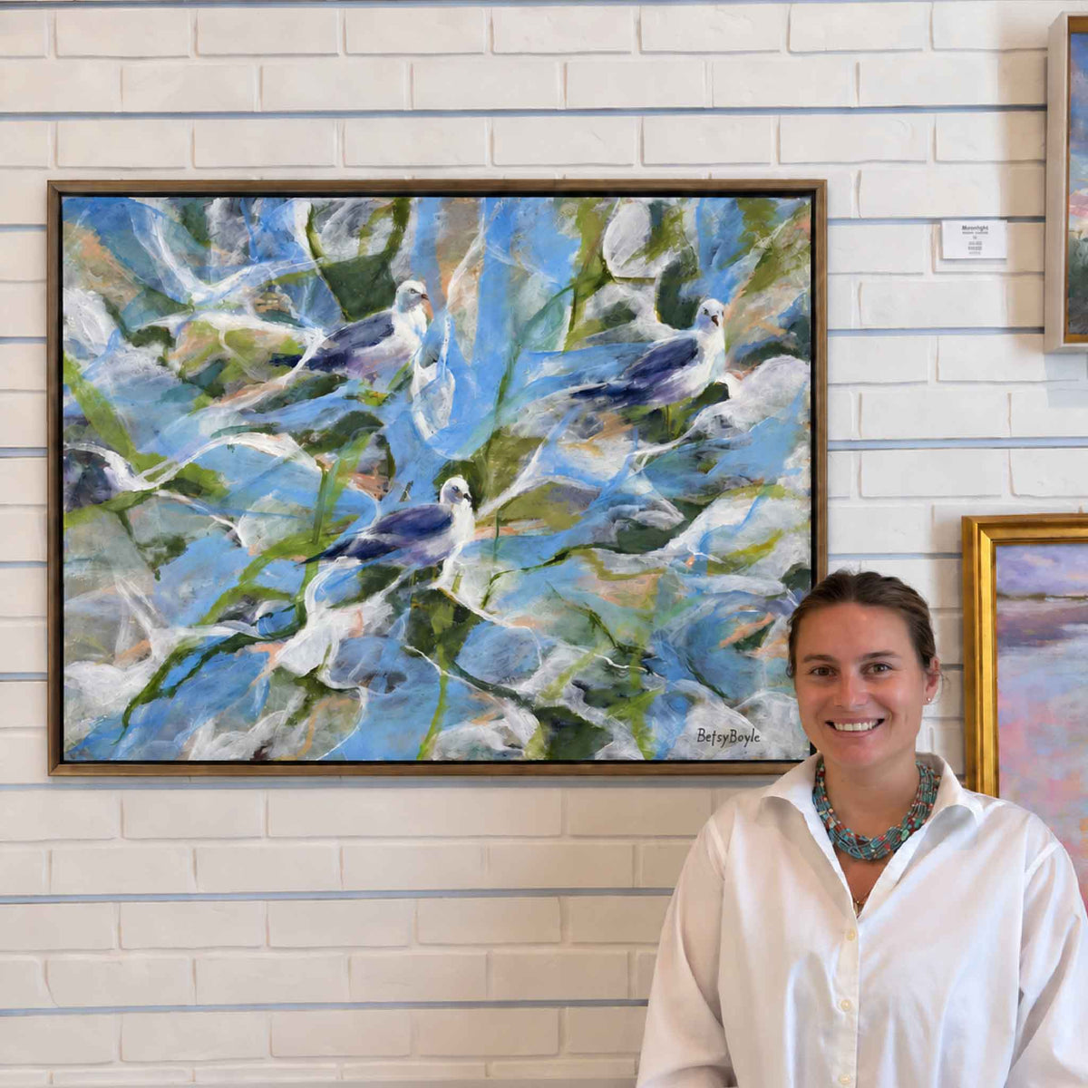 Kyra standing by “Never in a Frenzy,” an original oil painting by local artist Betsy Boyle at Gray Man Gallery in Pawleys Island, featuring coastal birds in expressive, modern Lowcountry style