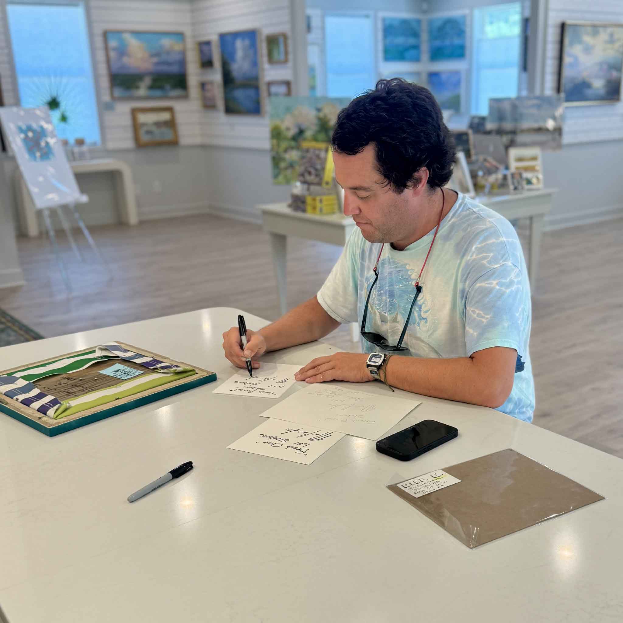 Charleston artist Nick kawczynski working by hand on original pen and watercolor artwork at Gray Man Gallery in Pawleys Island, South Carolina, showing the artist and handmade process behind French Parasol + Shibumi.