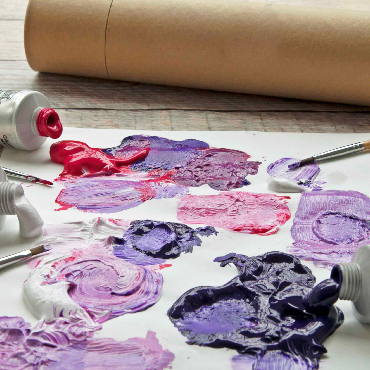 Artist’s palette covered in vibrant pink, purple and red oil paints with brushes and paint tubes, representing the collection of original art under $500 available at Gray Man Gallery in Pawleys Island, South Carolina.