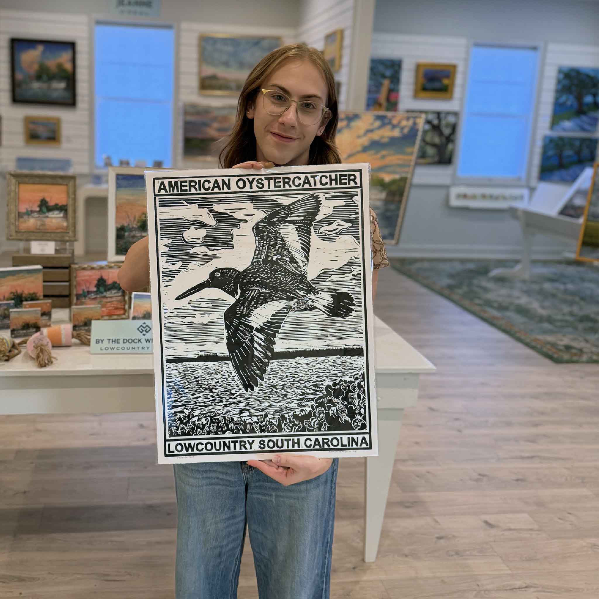 Alex holding the black Oystercatcher linocut print by Aaron Baldwin inside Gray Man Gallery.