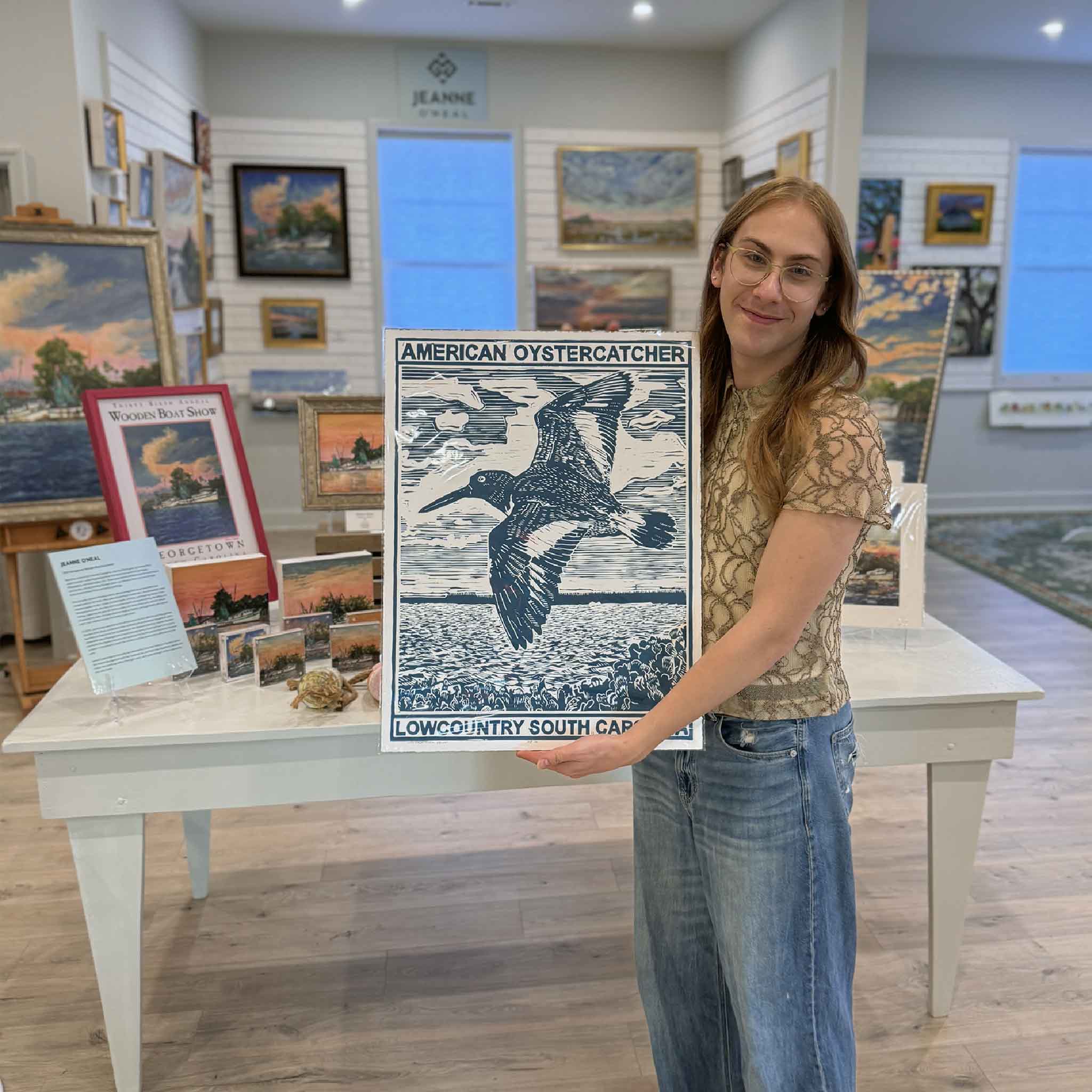 Alex holding the blue Oystercatcher linocut print by Aaron Baldwin at Gray Man Gallery in Pawleys Island.
