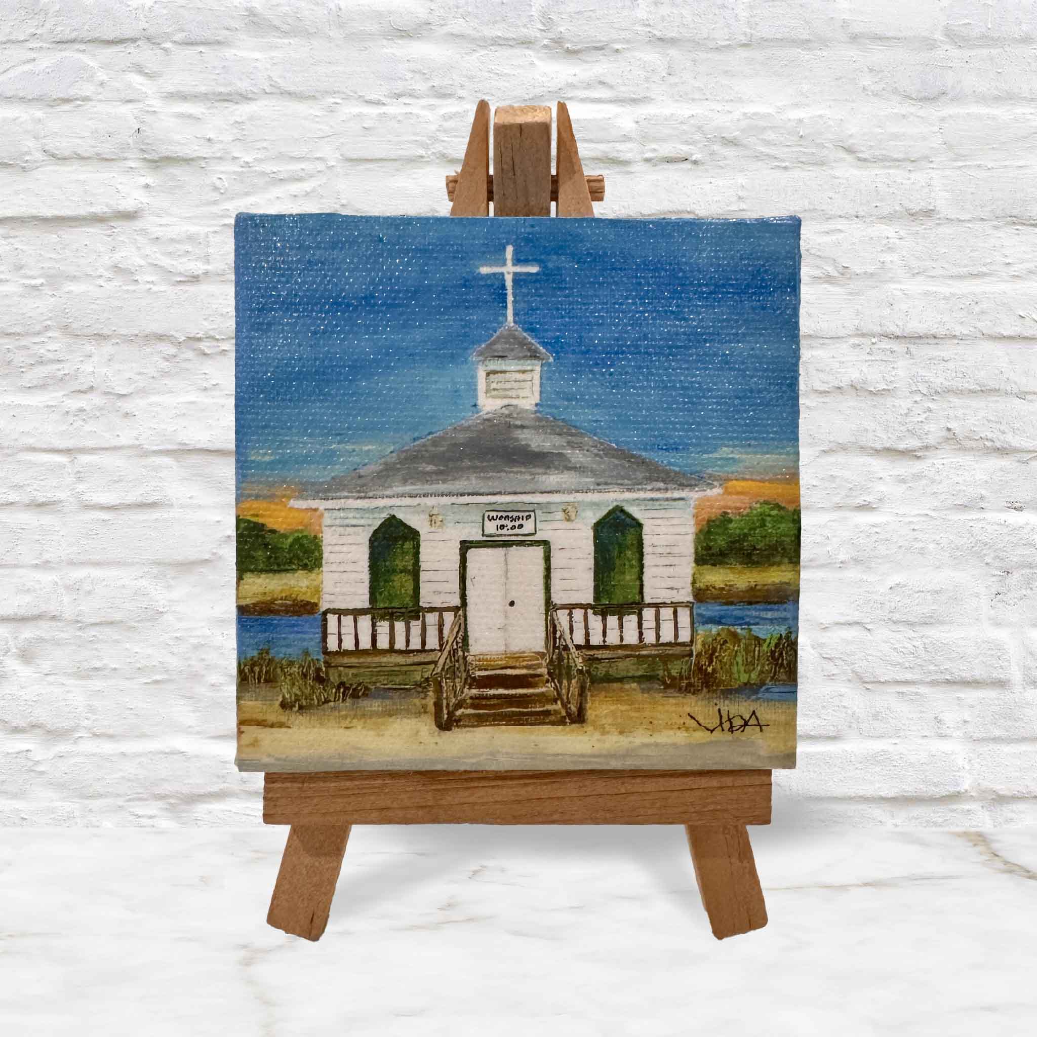 Pawleys Island Chapel mini canvas by local artist Vida Miller, depicting the iconic white island chapel with steeple and cross against a Lowcountry sky, displayed on a wooden easel and available at Gray Man Gallery in Pawleys Island, South Carolina