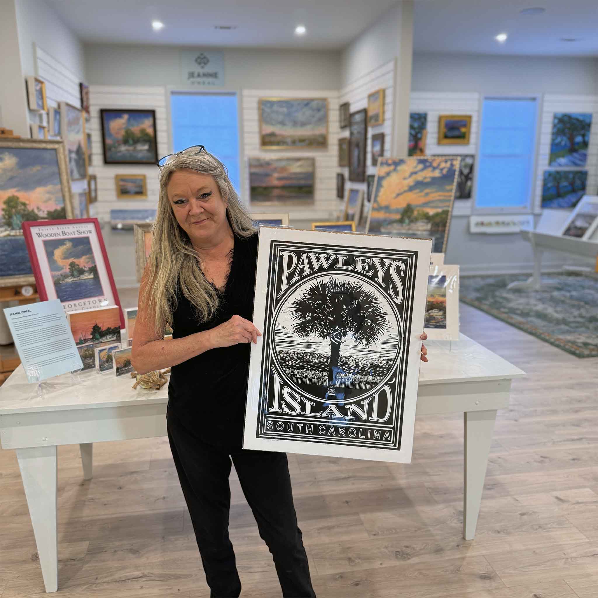 Jeanne holding the black Pawleys Island linocut print by Aaron Baldwin inside Gray Man Gallery.