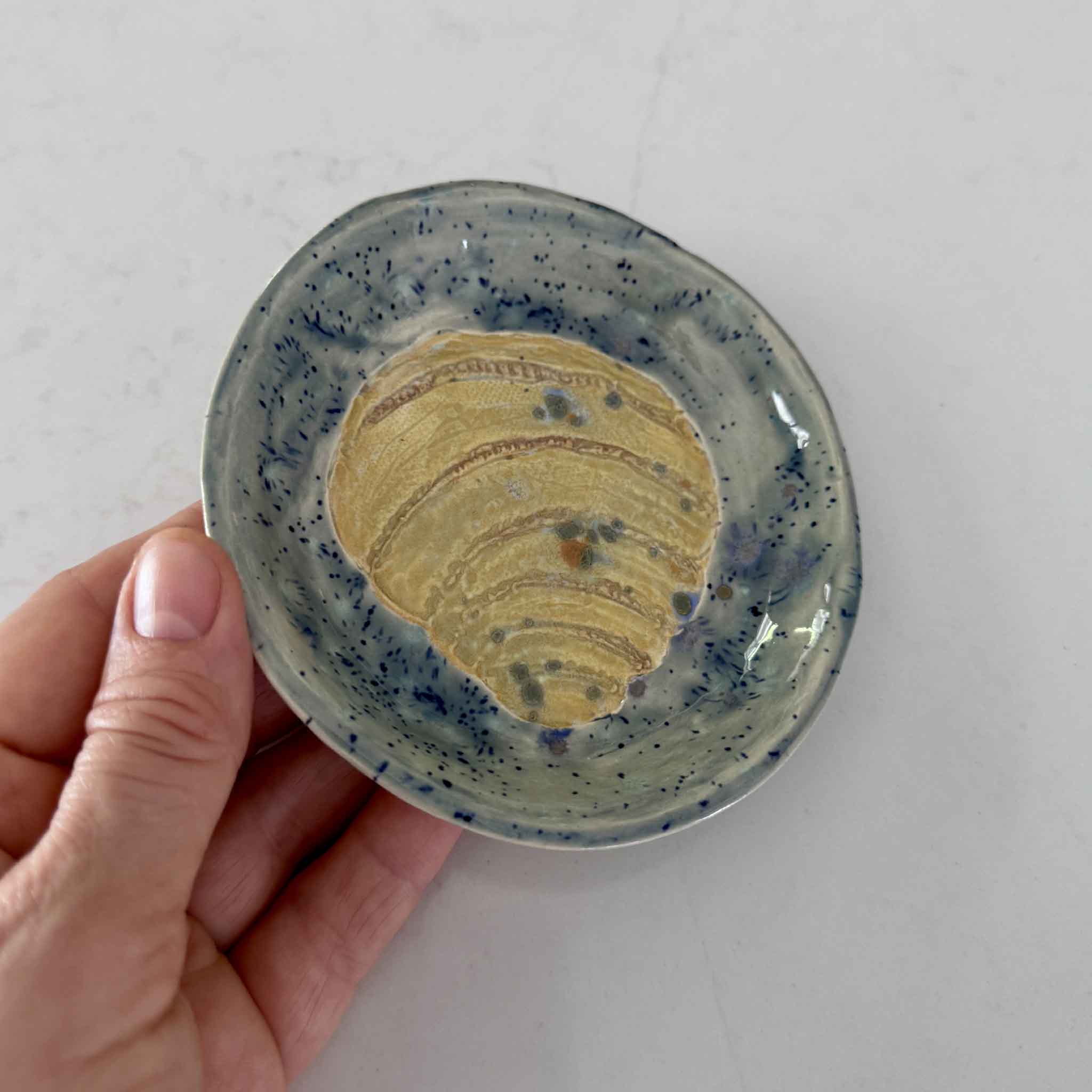 A handcrafted blue ceramic dish by Vida Miller is shown in hand, highlighting the carved Pawleys Island shell and speckled coastal glaze.